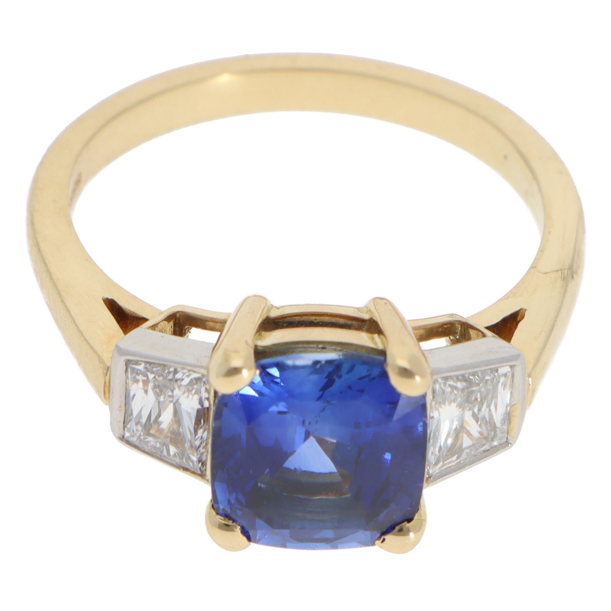 A beautiful blue sapphire and diamond three stone ring set in 18k yellow and white gold.

The piece is predominantly set with an astounding 3.00 carat cushion cut sapphire which is securely four claw set to centre. To either side of the central