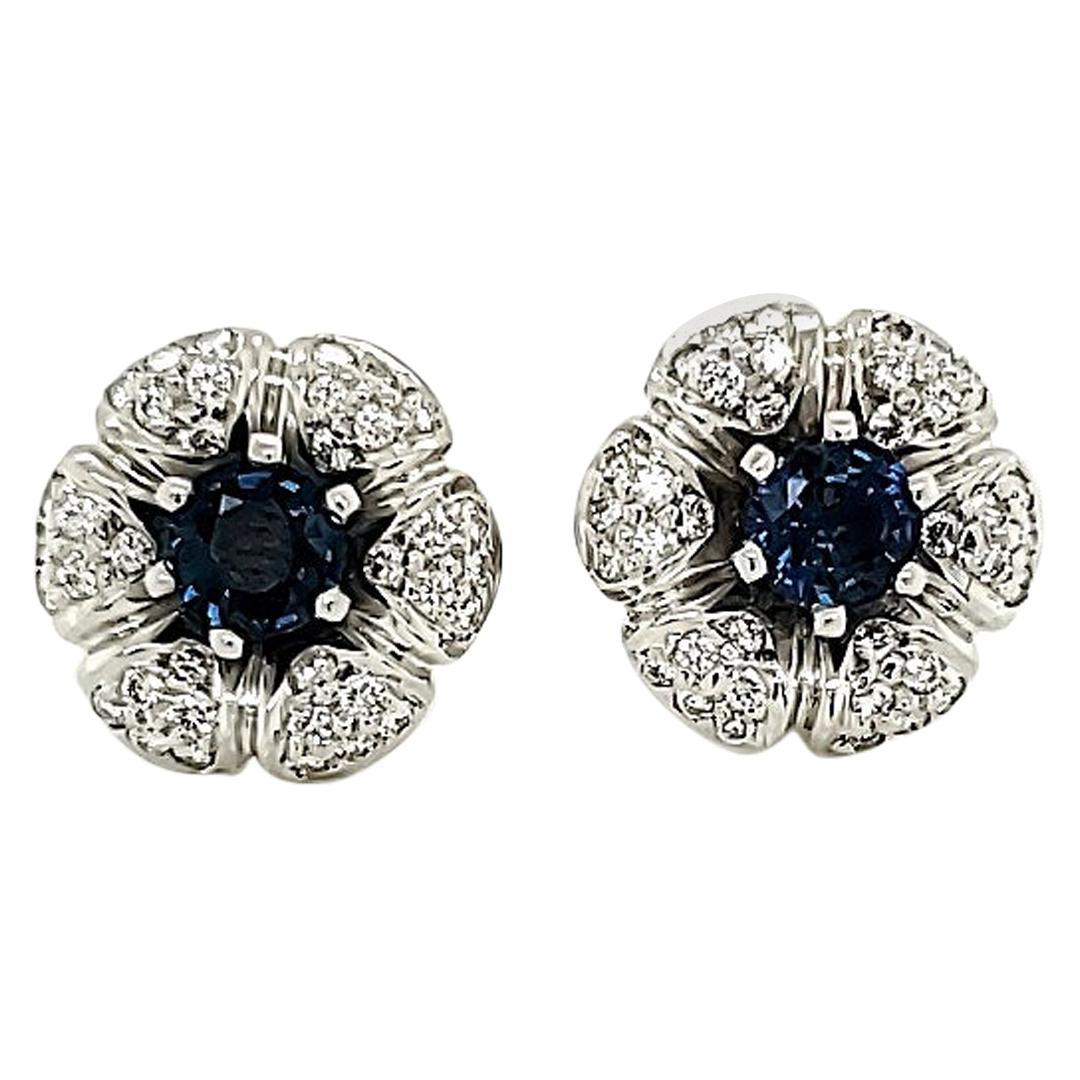 Blue Sapphire And Diamond White Gold Stud Earrings: 

Round Blue Sapphires weighing a total of 1.10 carat, surrounded by White Diamonds in a floral pattern weighing a total of 0.60 carat, to be worn as studs. The earrings are crafted in 18K White