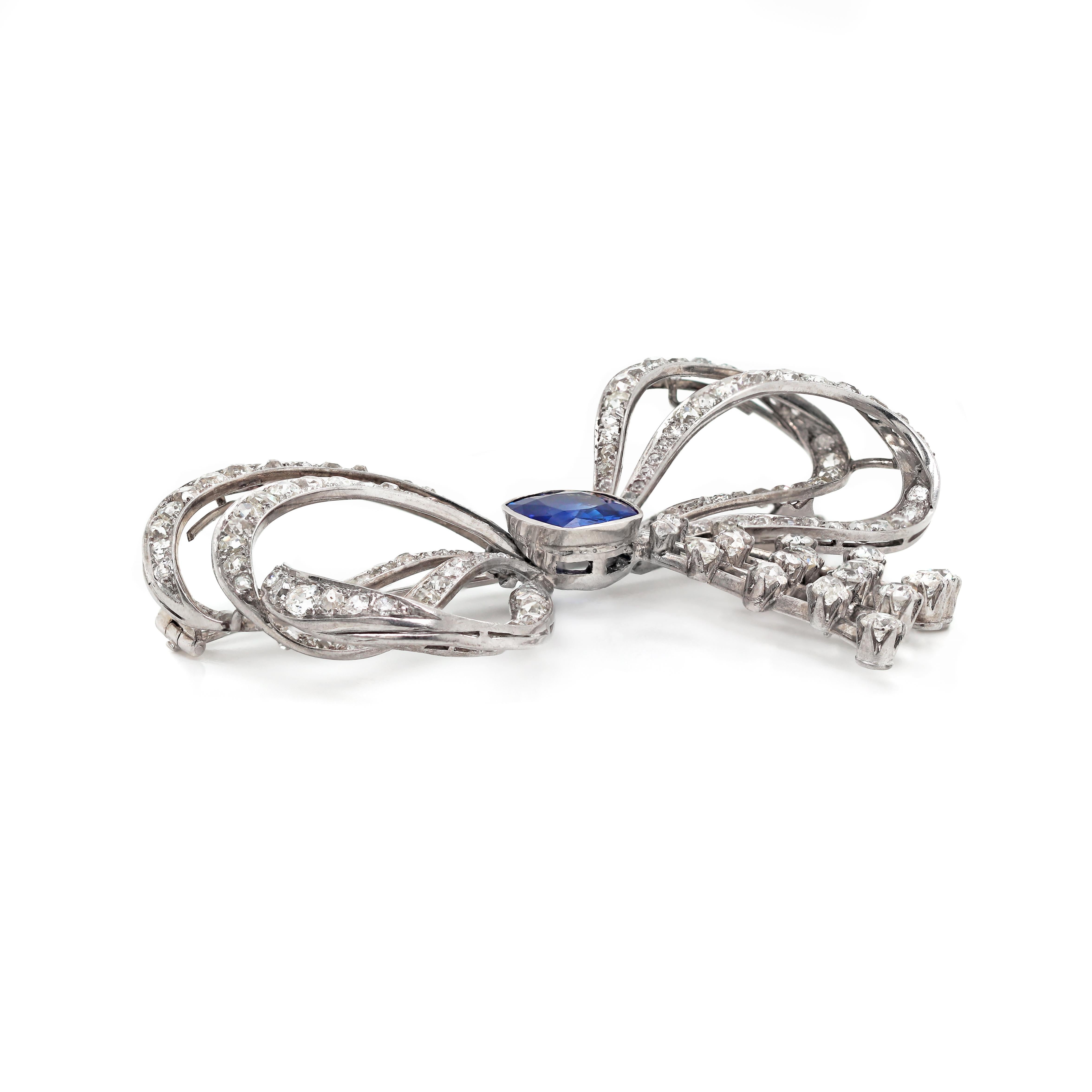 This exceptional 1930's handmade brooch/ pendant features a cushion shaped blue sapphire weighing approximately 5.00ct in an open back, rub over setting, mounted in the centre of a bow. The ribbons are pavé set with 136 old mine cut diamonds and the