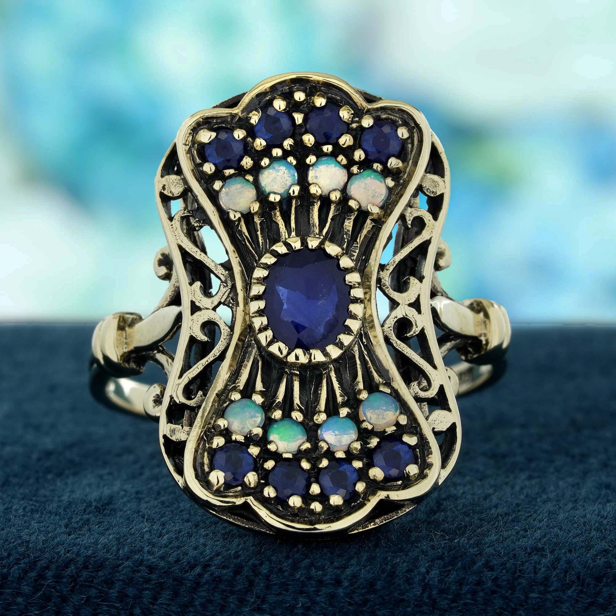 Este exquisito anillo de cóctel de estilo vintage se inspira en la grácil elegancia de una pluma de pavo real, con un llamativo zafiro azul natural en su centro. Alrededor del zafiro hay ópalos brillantes que imitan los delicados matices del penacho