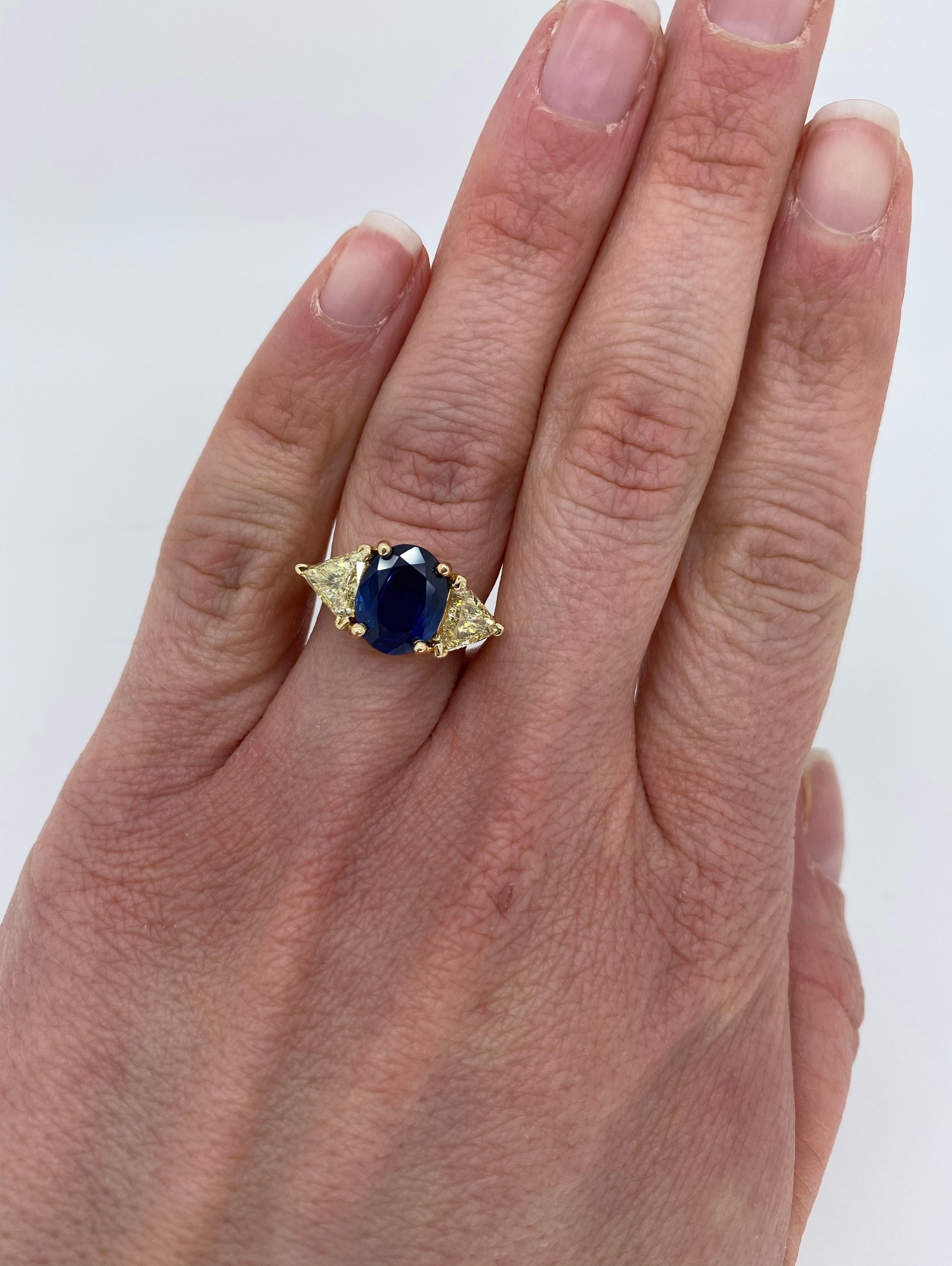 Unique Blue Sapphire and light yellow diamond ring crafted in 14k yellow gold.

Gemstone: Blue Sapphire & Diamond
Gemstone Carat Weight: Approximately 10.12mm x 8.25mm Oval Cut 
Diamond Cut: Trilliant Cut Diamonds
Average Diamond Color: Light