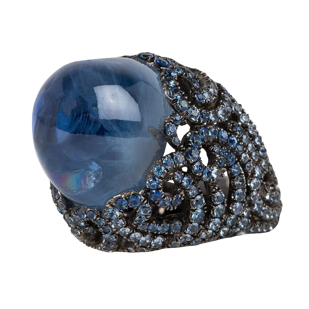 This sapphire is appx 28 carat and originates from Sri Lanka.
This cabochon stone is surrounded by round sapphire stones in an elaborate setting.
This sapphire stone is a medium blue color and is a natural unheated sapphire. 
The ring is set into