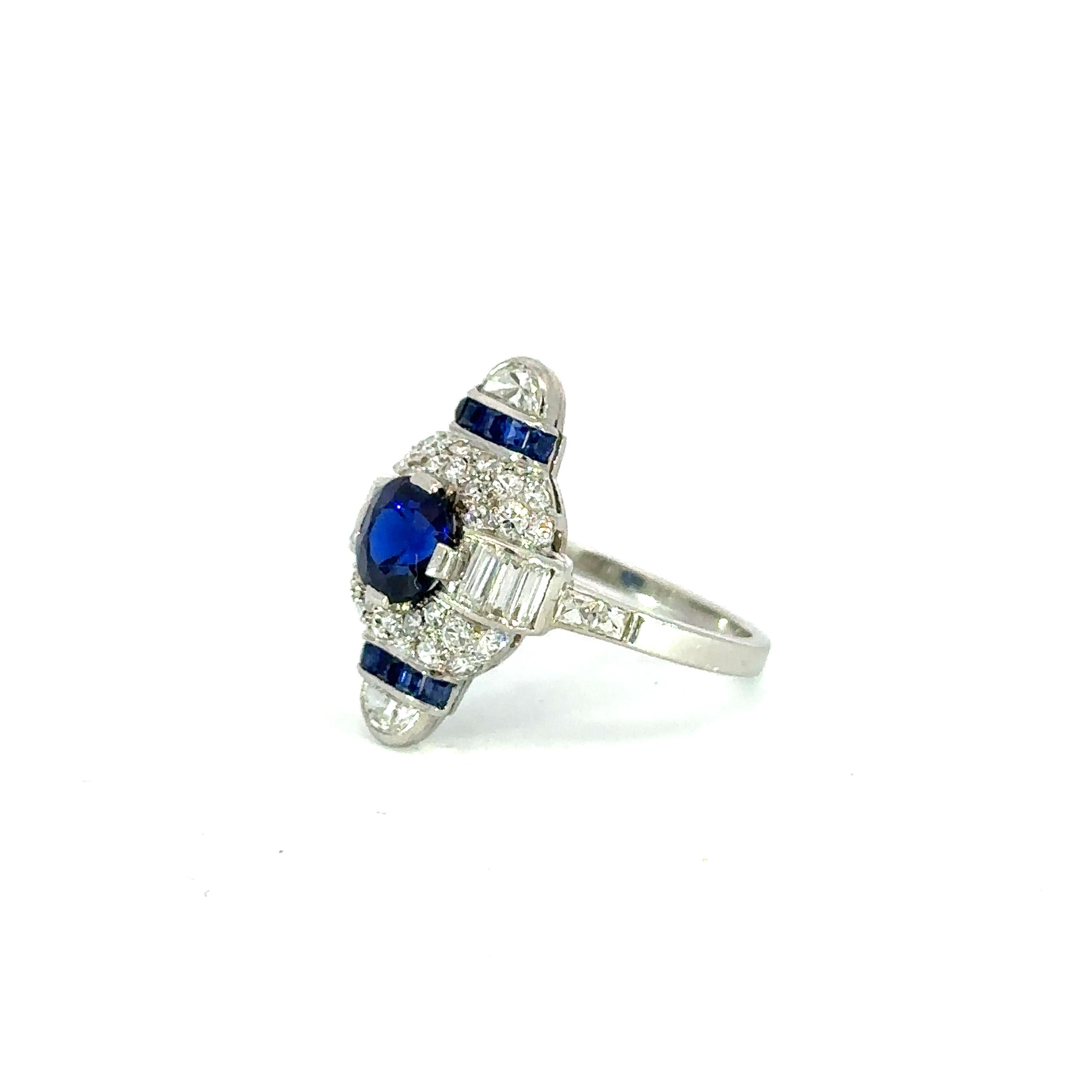 A blue sapphire Art Deco Cartier white gold cocktail ring boasts a captivating deep blue sapphire at its center, encircled by diamonds. Its design showcases geometric shapes, intricate filigree, and milgrain detailing. The white gold setting exudes