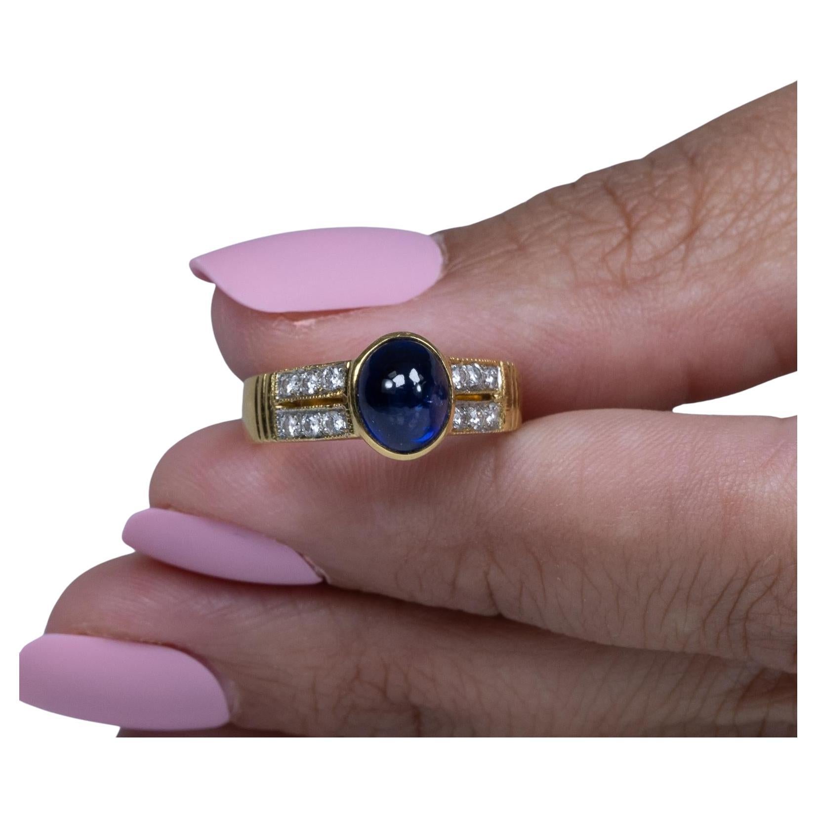 This exquisite ring features a captivating blue sapphire cabochon, bezel-set to highlight its smooth, polished surface. Framed by a split shank adorned with sparkling diamonds, the design combines modern elegance with classic charm. Crafted in 90%