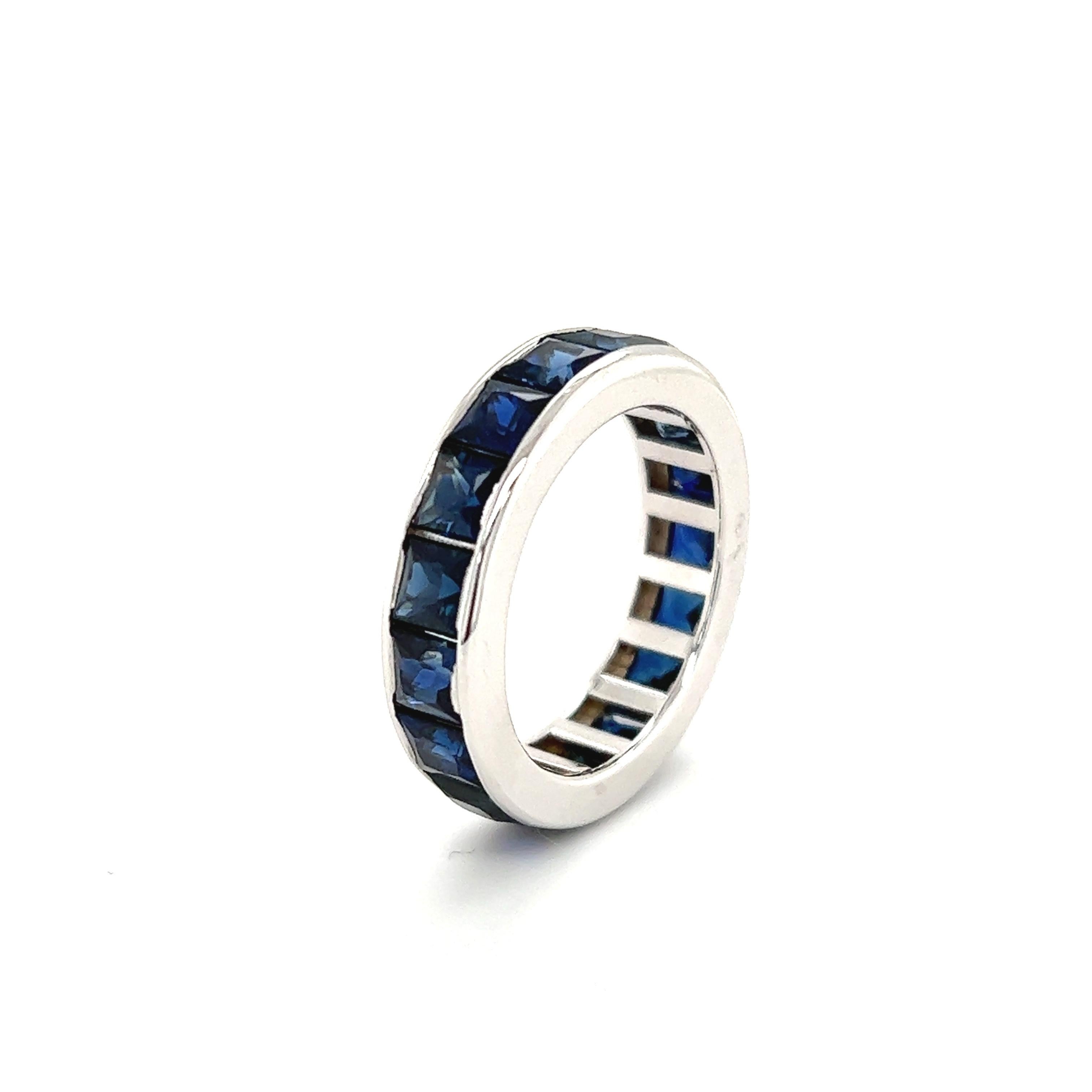 Gorgeous blue sapphire gemstone eternity band crafted in 18k white gold. The ring displays electric colored blue sapphires that pop off this one of a kind creation. There are 18 sapphires set in the ring, all princess cut gemstones that are matched