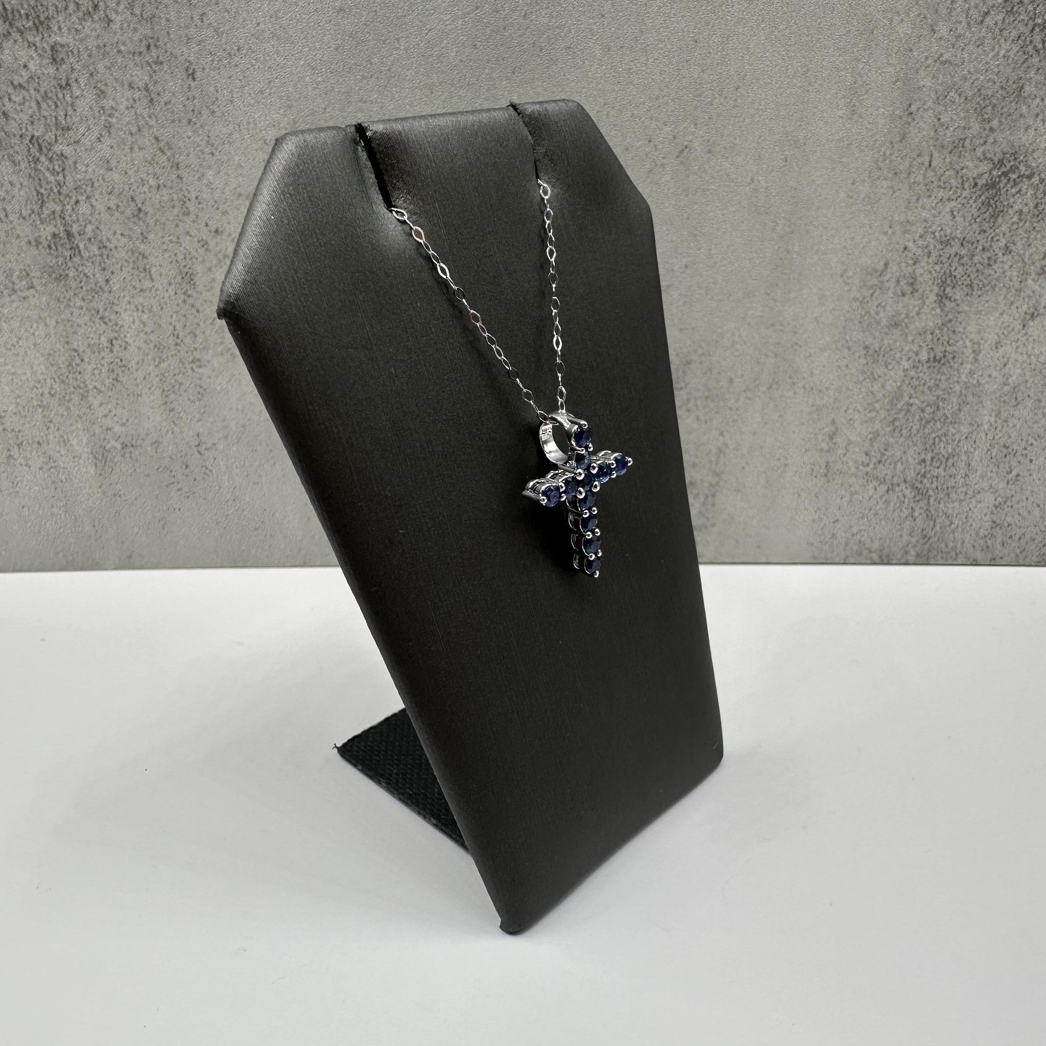 Ce magnifique collier croix en saphir bleu en or blanc 14kt présente un poids total de 0,88 carats de saphirs bleus ronds sertis dans un design de croix intemporel. Les teintes bleues profondes des saphirs contrastent élégamment avec l'or blanc