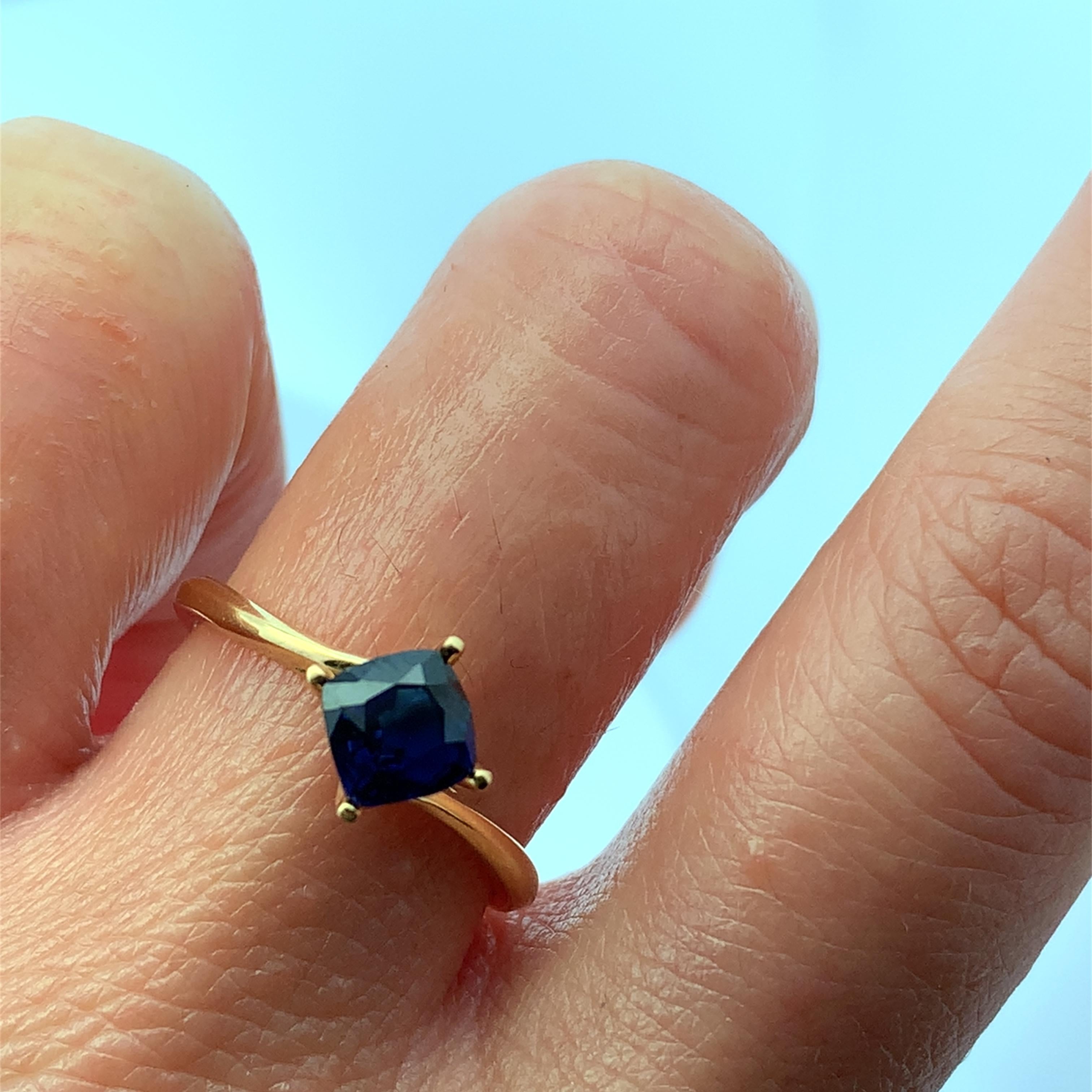 Entdecken Sie die Anziehungskraft dieses eleganten Goldrings mit einem atemberaubenden tiefblauen Saphir im Kissenschliff in seiner Mitte. Das einzigartige Design verbindet moderne Ästhetik mit zeitloser Eleganz und ist damit ein perfektes