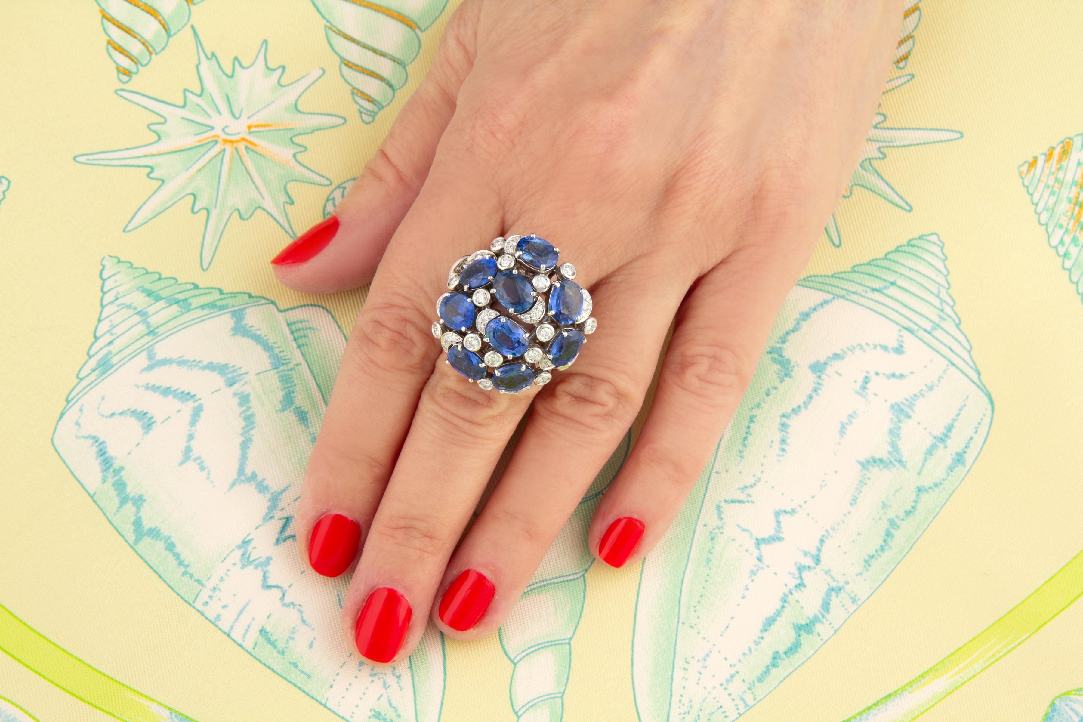 El anillo de cóctel de zafiro azul y cúpula de diamantes presenta 11,97 quilates de zafiros de Ceilán facetados de calidad y talla ovalada. Los zafiros están artísticamente engastados en un sofisticado diseño floral que lleva 1,98 quilates de
