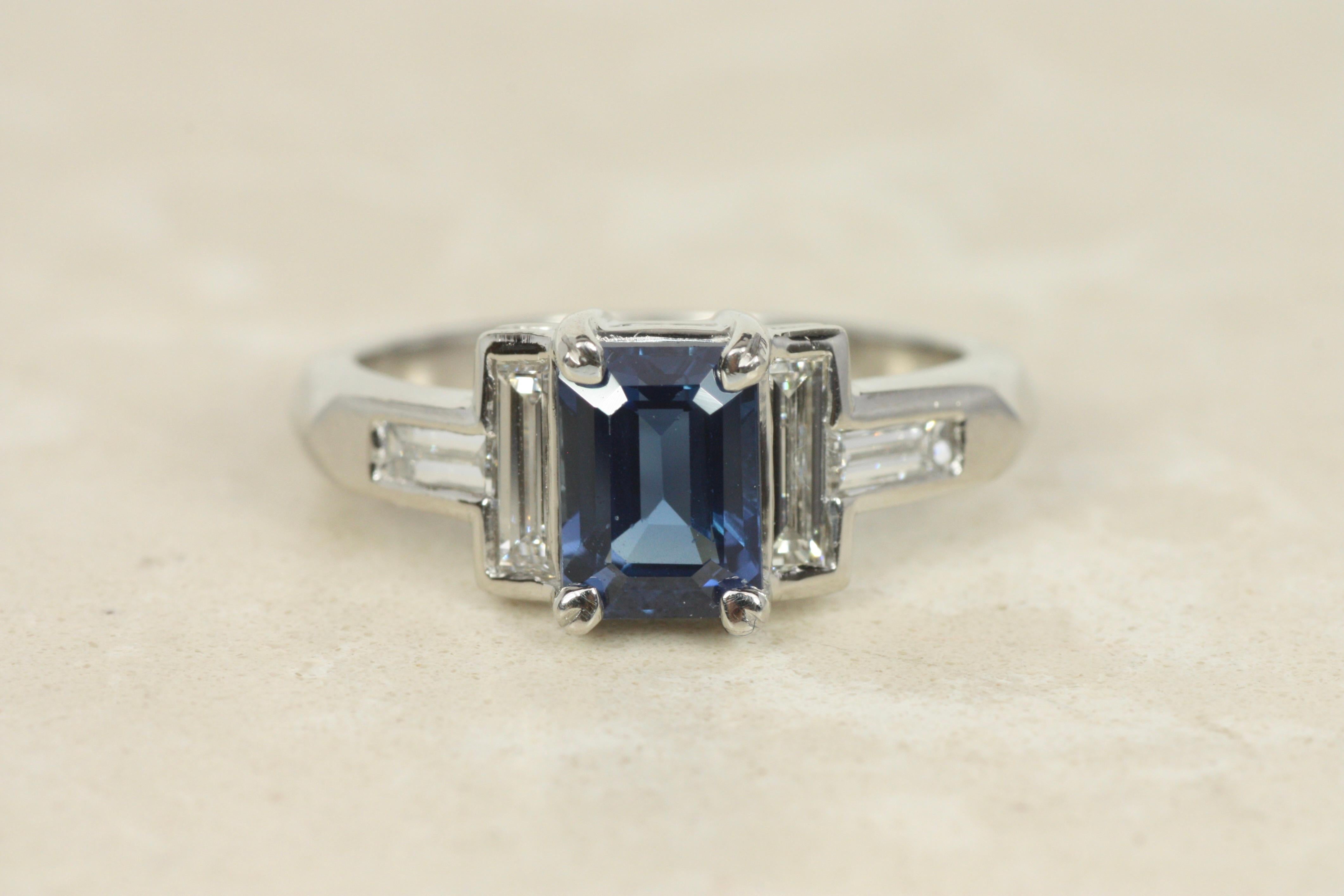 This striking engagement ring combines classic sophistication with a modern aesthetic. At its center is a 1.52ct emerald-cut blue sapphire, prized for its rich hue and elegant proportions. Flanking the sapphire are four baguette-cut diamonds