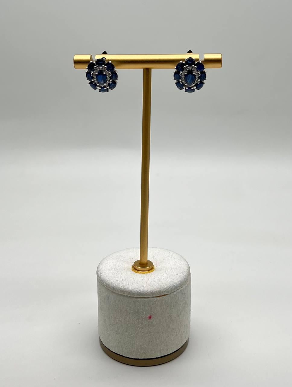 Estos elegantes pendientes presentan un óvalo central de zafiros azules rodeado de un halo de piedras azules más pequeñas, creando un motivo floral. El intrincado diseño está engastado en un metal pulido que realza los tonos vibrantes de las