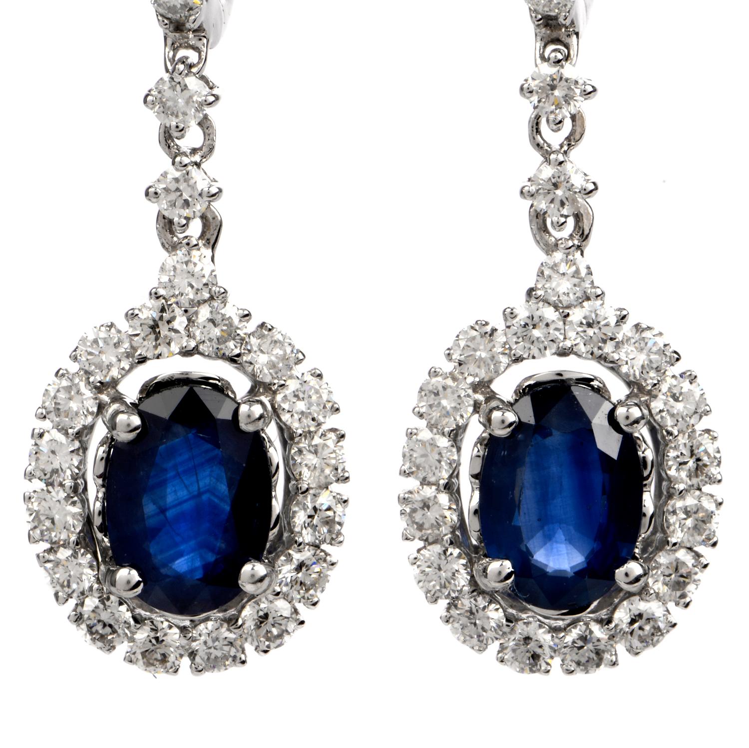 These stunning diamond and blue sapphire half hoop dangle drop earrings are crafted in solid 18 karat white gold. Displaying a pair of prominent oval shaped prong-set blue sapphires, collectively weighing, 1.94 carats. Surrounded by a 54 round-cut