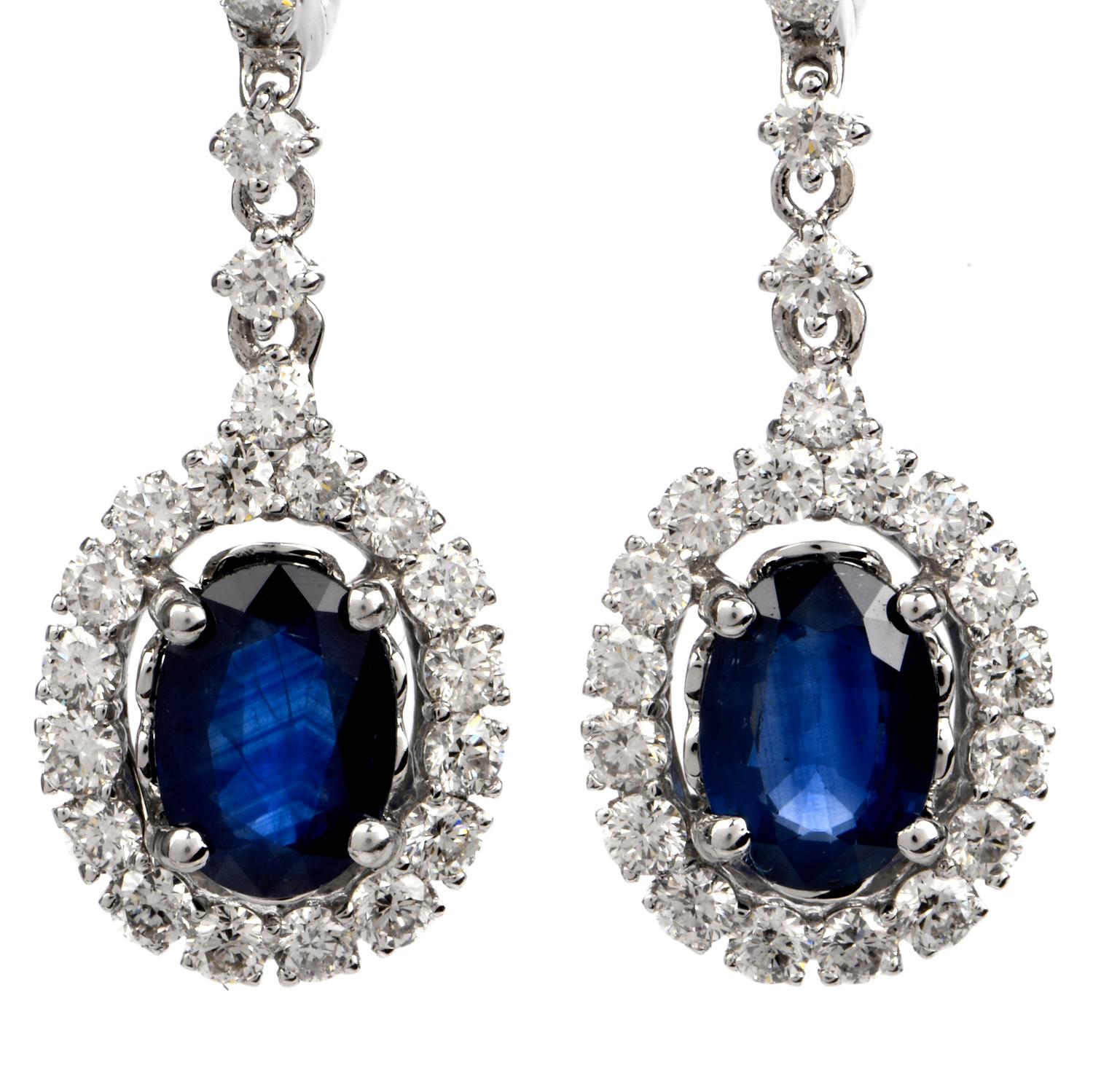 These stunning diamond and blue sapphire half hoop dangle drop earrings are crafted in solid 18 karat white gold. Displaying a pair of prominent oval shaped prong-set blue sapphires, collectively weighing, 1.94 carats. Surrounded by a 54 round-cut