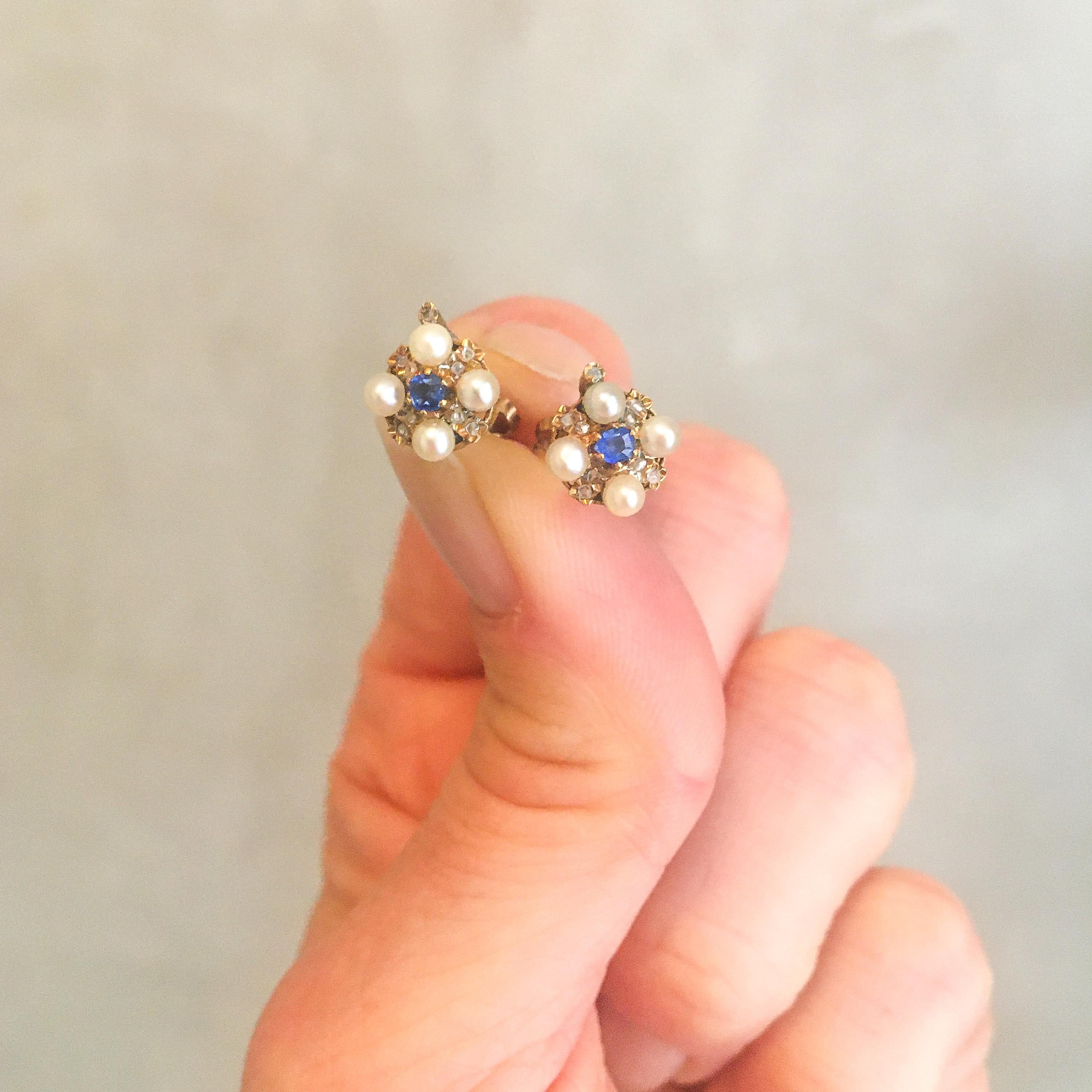 These lovely early 20th century stud earrings are made of 14 karat gold. The earrings are set with one blue sapphire in the middle, surrounded by four cultured pearls and eight small old cut diamonds. On top of the earrings, one diamond rises