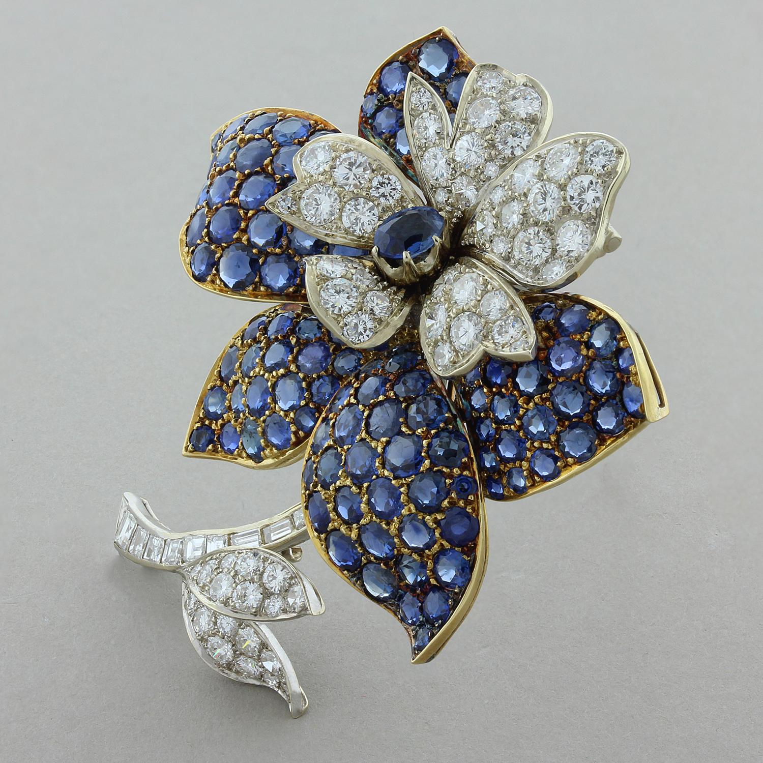 This exquisite flower blossom features 12 carats of round cut blue sapphires set in 18K yellow gold that make up the outer petals the flower. The center of the flower is detailed with five smaller diamond petals and a diamond stem with two leaves on