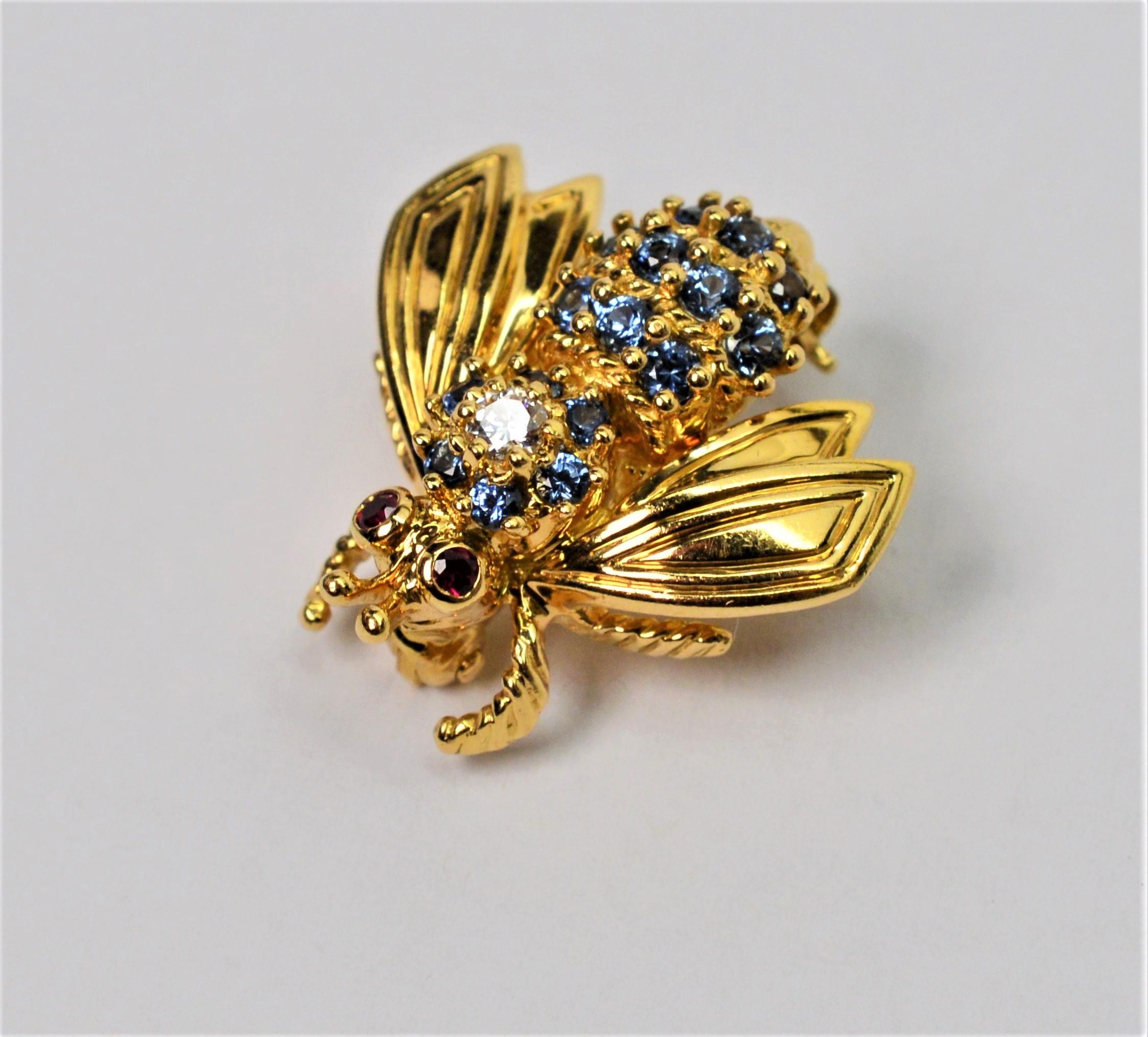 Charming and collectable by Tiffany & Company. This adorable Bee Pin Brooch in bright eighteen karat yellow gold 18k is adorned with sixteen blue sapphires and crowned with one .05 carat white diamond along the body and tiny ruby eyes. Our little