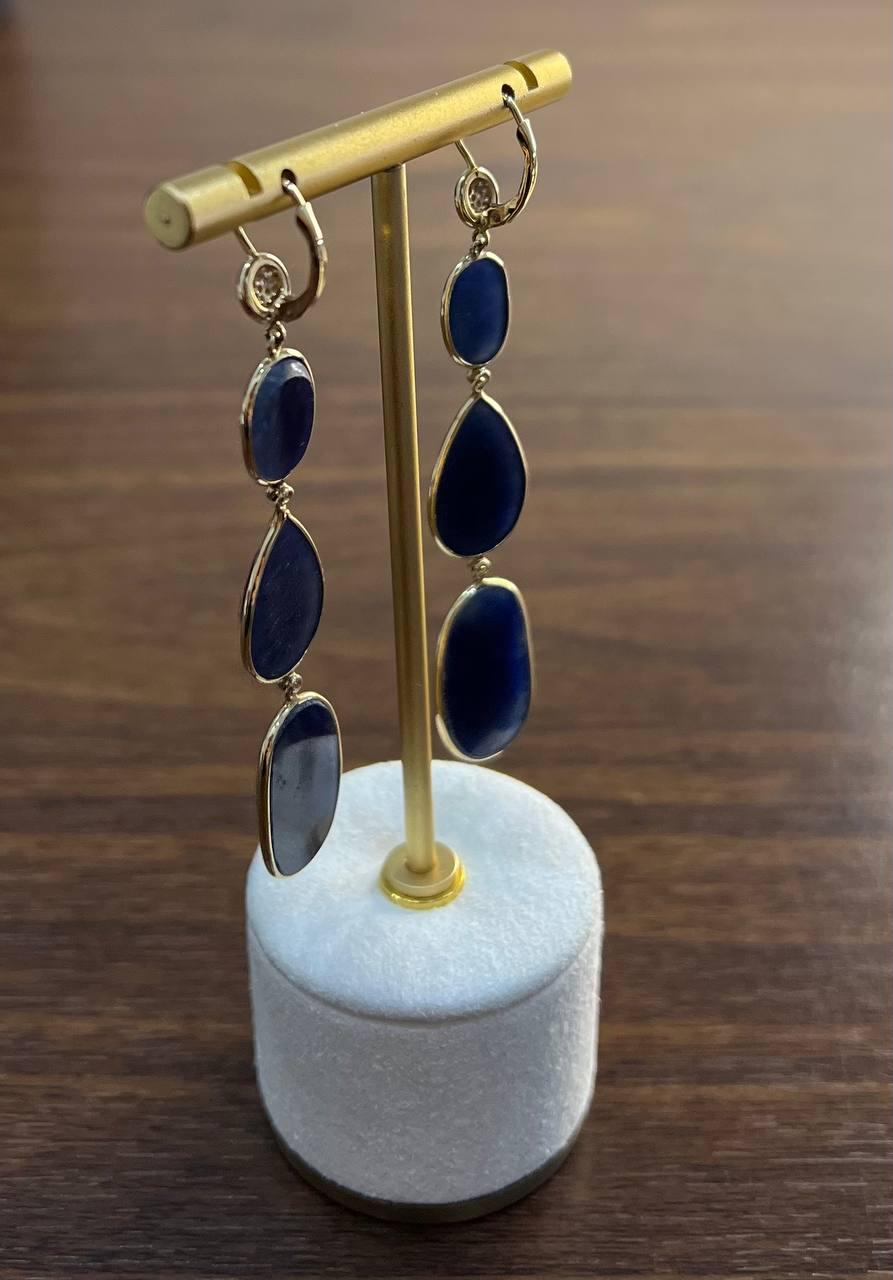 Eleganti orecchini a goccia con pietre preziose. Questi straordinari orecchini presentano un design sofisticato con una combinazione di fette di zaffiro blu scuro sfaccettate e lisce.

Ogni orecchino inizia con un piccolo diamante rotondo