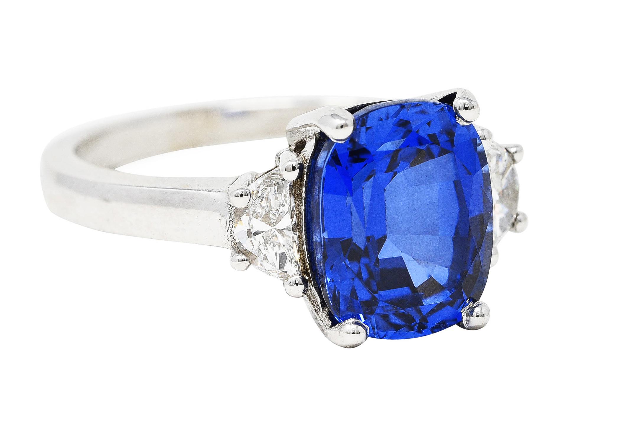 Centering a rectangular cushion cut sapphire weighing approximately 5.05 carats total. Transparent medium blue in color - prong set and flanked by half-moon cut diamonds. Weighing approximately 0.38 carat total - G color with VS clarity. Stamped 14k