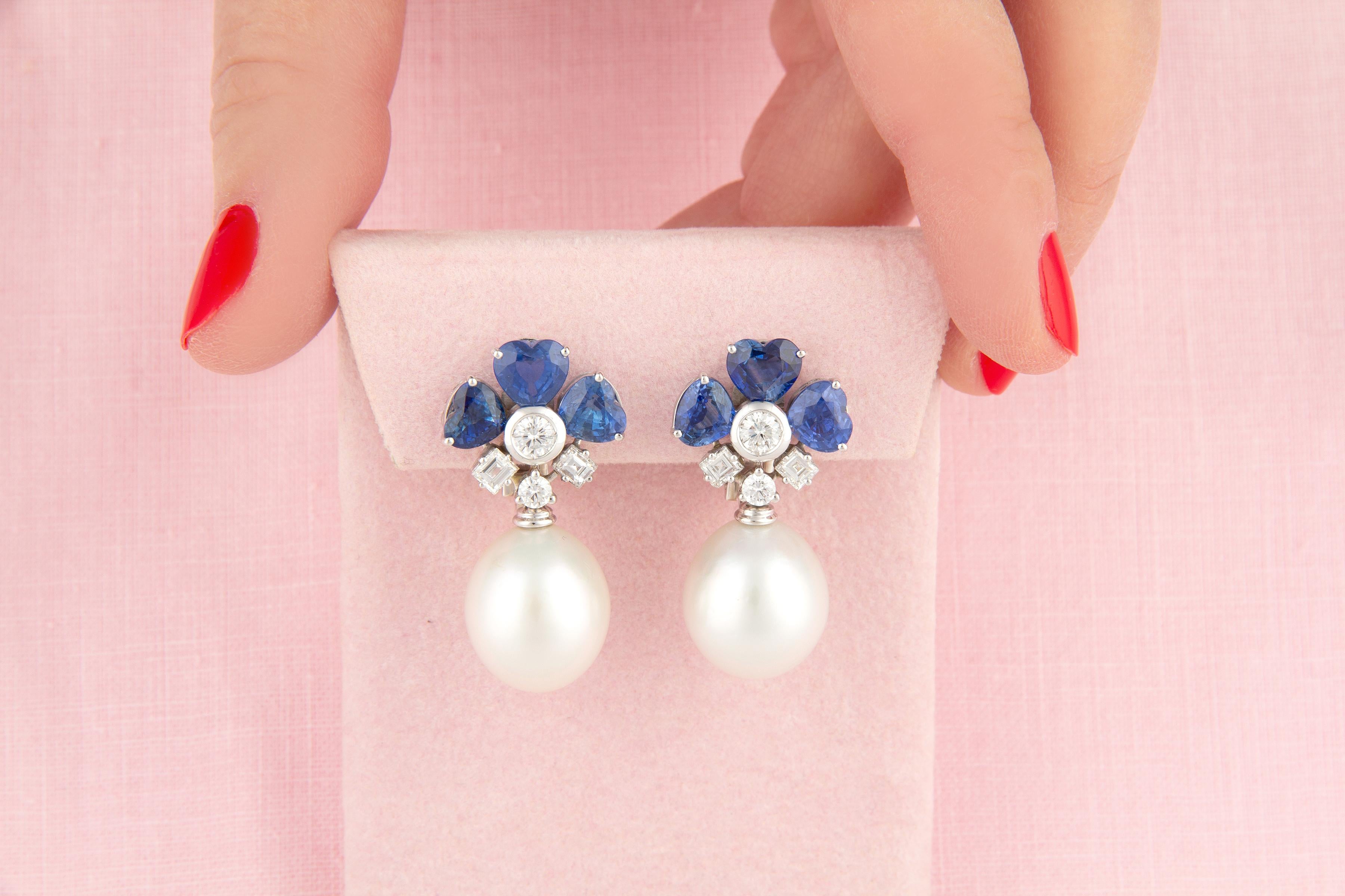 This pair of blue sapphire heart shape and pearl earrings features a design on the ear with 8.85 carats of oval cut faceted Ceylon sapphires of brilliant blue color. The tops suspend 2 South Sea pearls of 16.5 x 13mm diameter. The design is complete