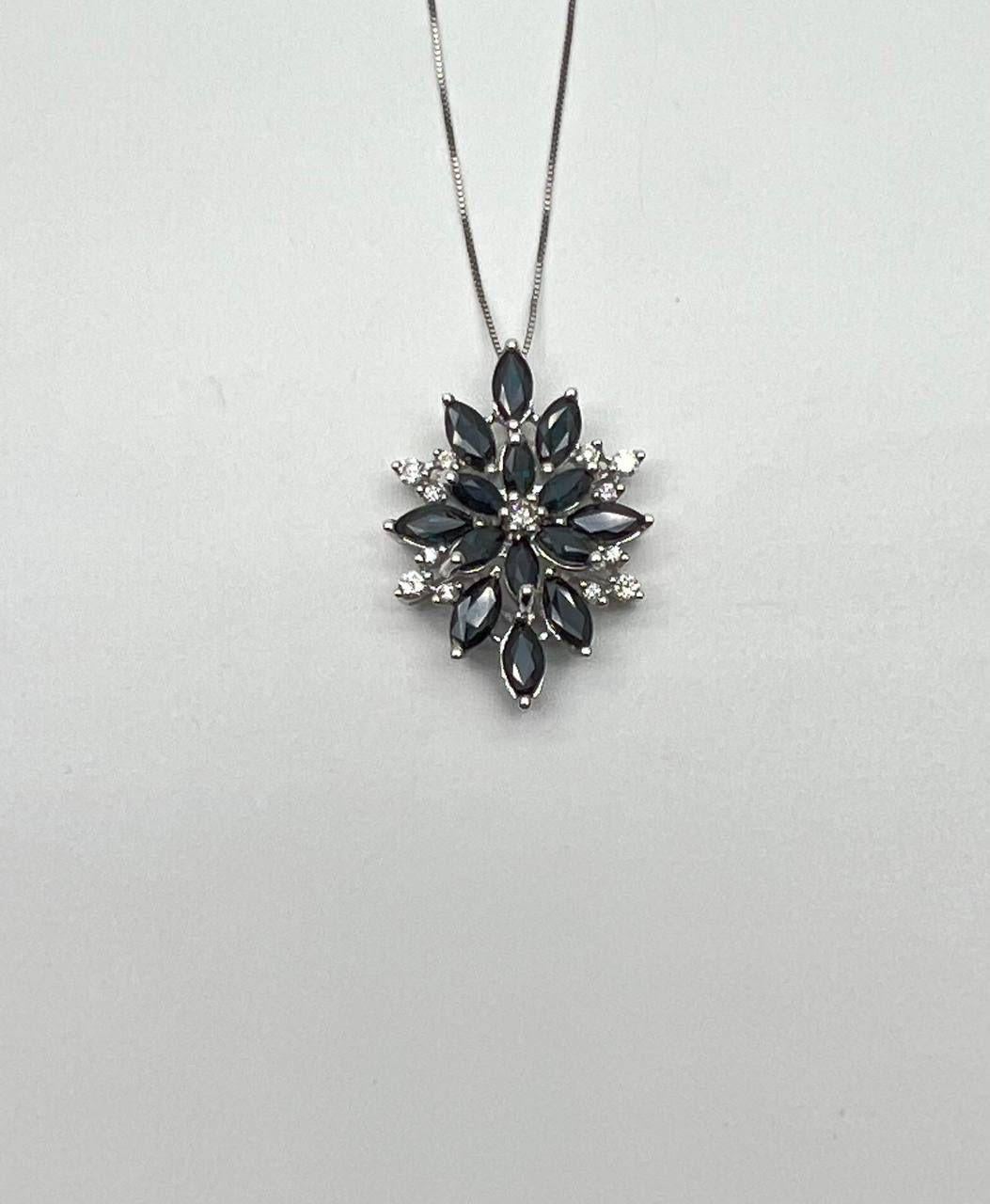 A striking pendant necklace, featuring a captivating design with marquise-cut dark blue sapphires and sparkling round accent diamonds. This piece showcases a harmonious arrangement of stones, creating a floral motif. The pendant is suspended from a
