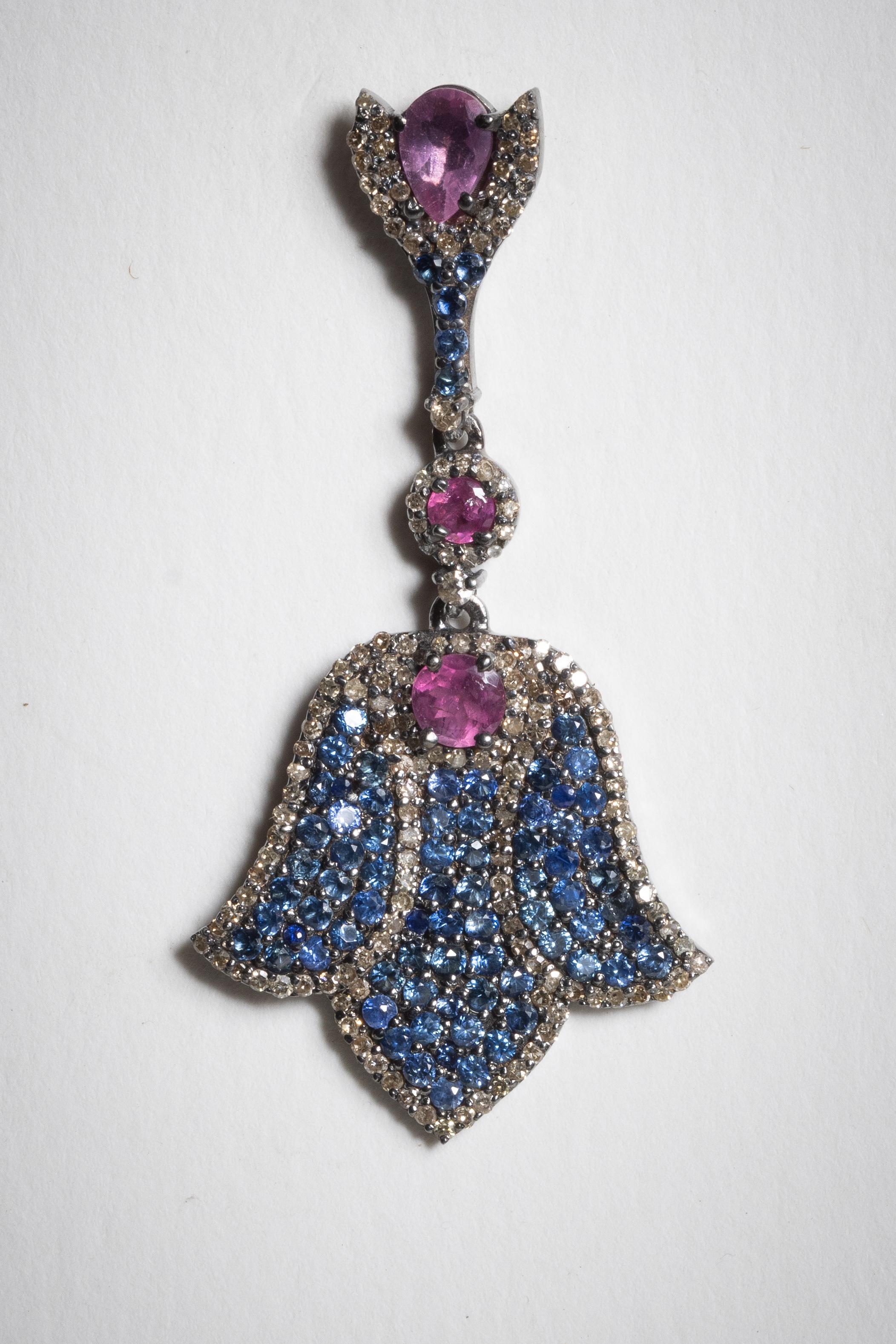 Si tratta di una splendida coppia di zaffiri rotondi taglio brillante incastonati in una montatura pave` con una linea di tormaline rosa sfaccettate al centro.  Sembrano quasi essere un capovolto  motivo del fiore di loto.  In argento sterling con