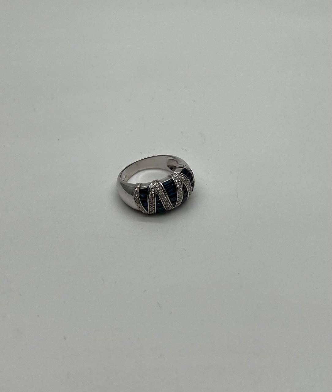 Crafted this exquisite piece features a bold design with alternating rows of deep blue sapphires and sparkling diamonds. The stones are set in a wide band, creating a captivating contrast that catches the eye. The band is smoothly polished,