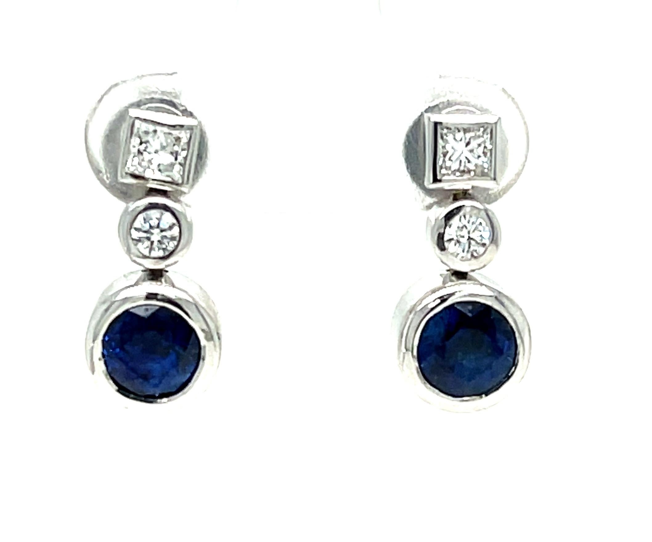 Cette paire de boucles d'oreilles, à la fois accrocheuse et subtile, présente un design élégant. Elles présentent une paire de saphirs bleus royaux magnifiquement assortis, surmontés de diamants ronds de taille princesse et de taille brillant,