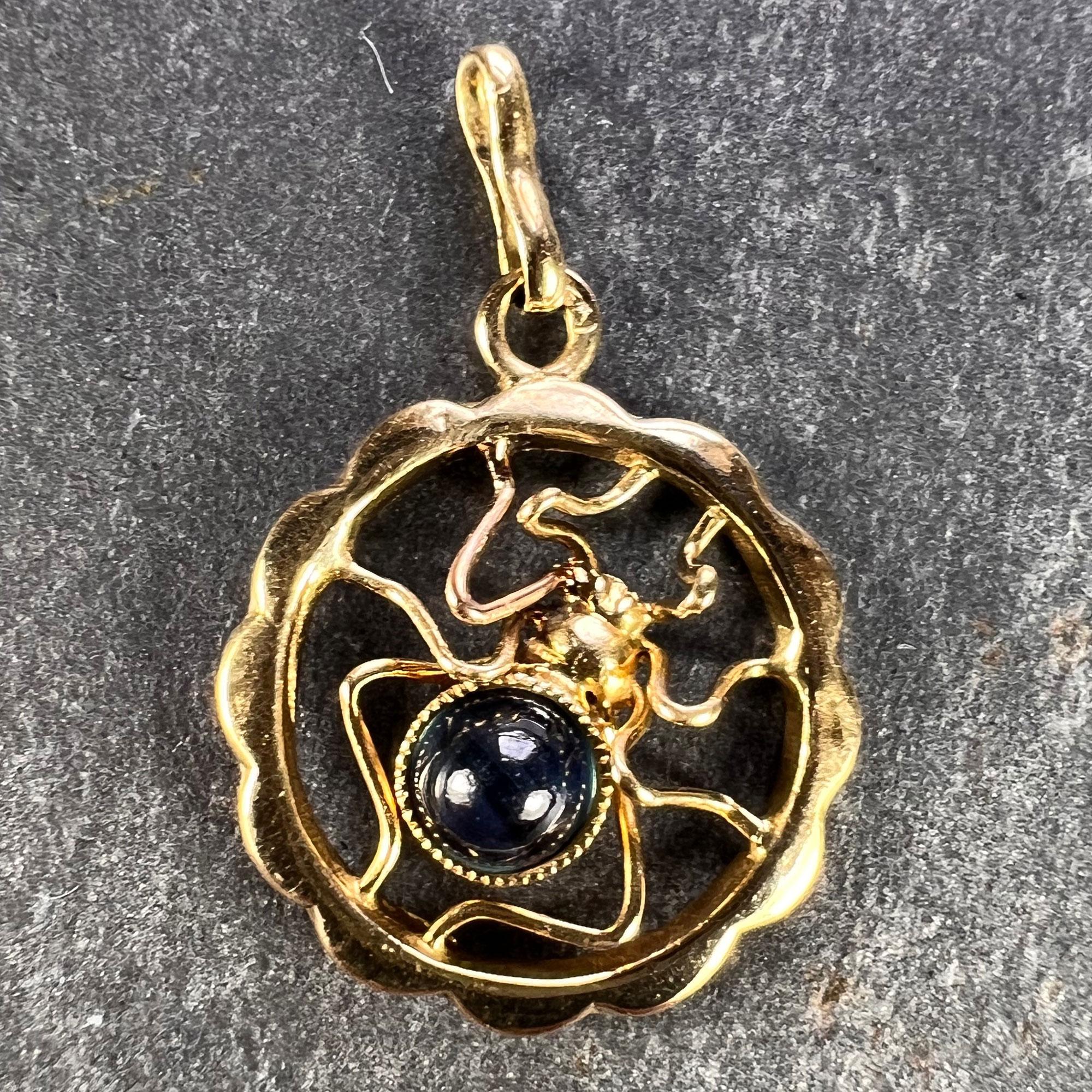 An 18K (18 karat) yellow gold charm pendant designed as an scalloped circle containing a gold spider with a cabochon blue sapphire body measuring 3.5 x 3.5 x. 2.9mm and weighing approximately 0.25 carats. Stamped 18K to the reverse with the French