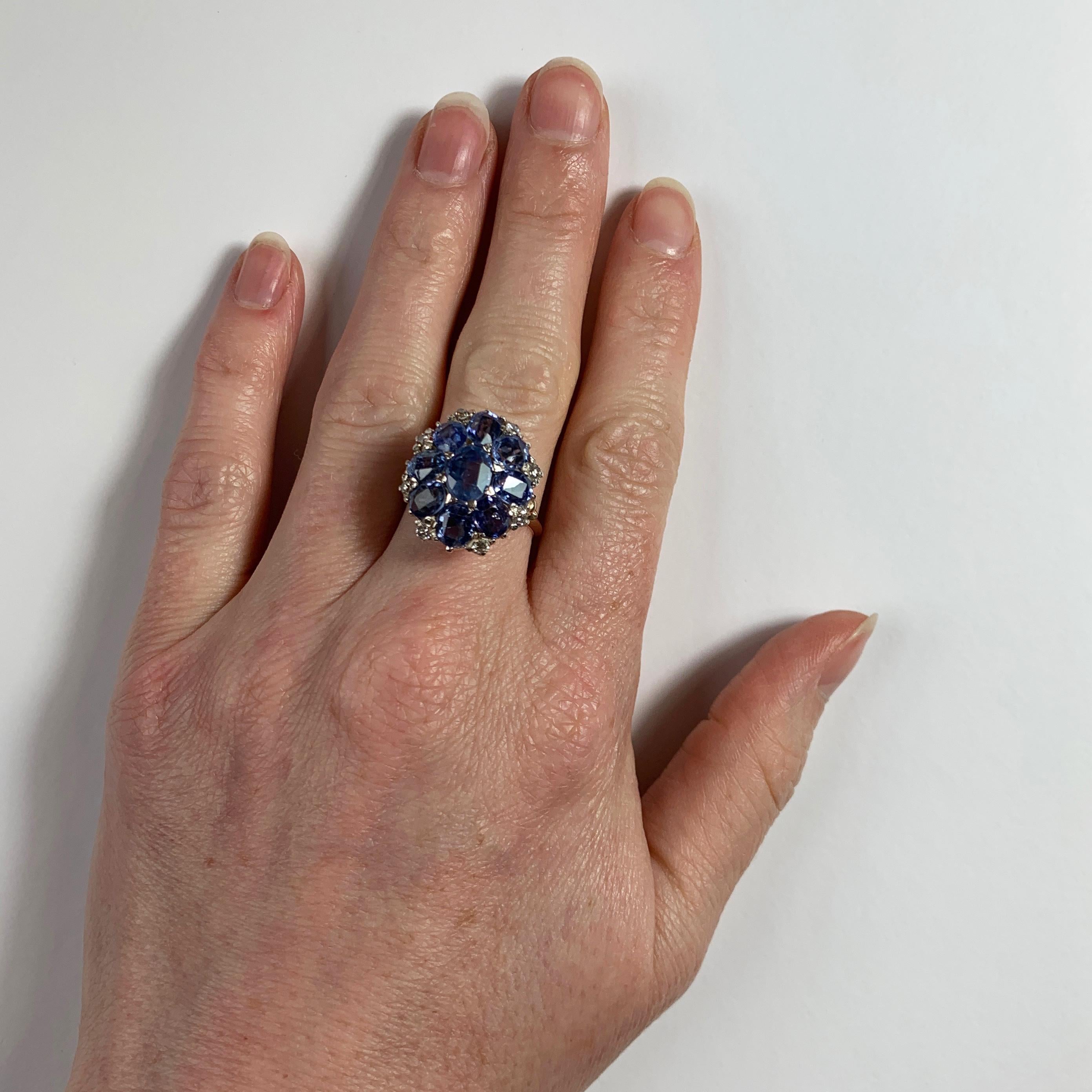 Ein Ring aus 18 Karat (18K) Weiß- und Roségold, besetzt mit neun ovalen blauen Saphiren und acht runden weißen Diamanten im Brillantschliff. Das Gewicht des mittleren Saphirs wird auf etwa 1,70 Karat geschätzt. Die Saphire weisen keine Anzeichen