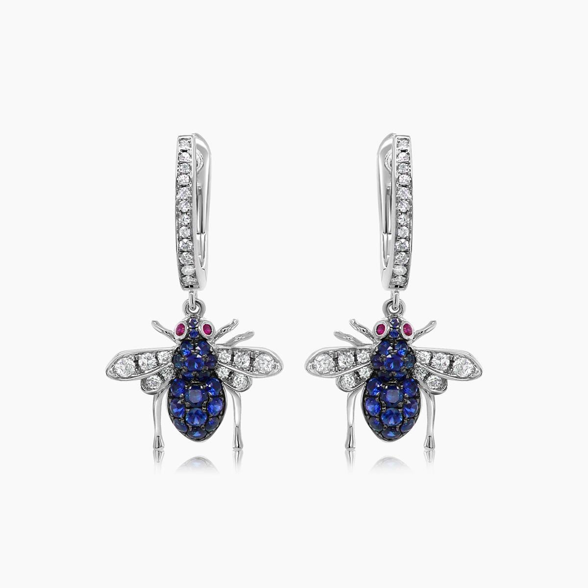 Diese exquisiten Ohrringe sind aus 18 Karat Weißgold gefertigt. Jeder Ohrring hat ein charmantes Insektenmotiv, das mit leuchtend blauen Saphiren und funkelnden weißen Diamanten verziert ist. Die Augen sind mit Rubinen verziert, die für einen Hauch