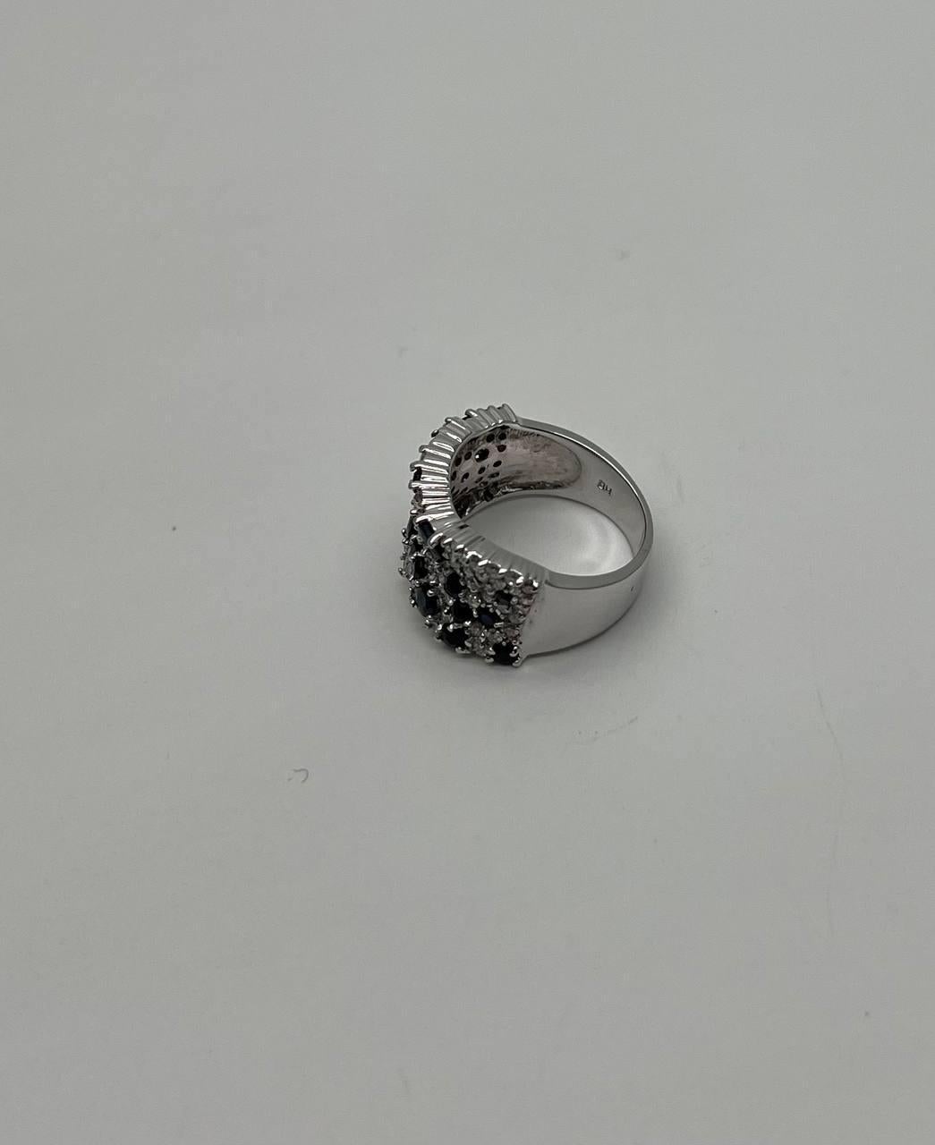 This exquisite ring is crafted in 14k white gold. The band features a stunning array of deep blue sapphires, interspersed with sparkling diamonds, creating a captivating pattern. The intricate design showcases a wide band with a textured surface,