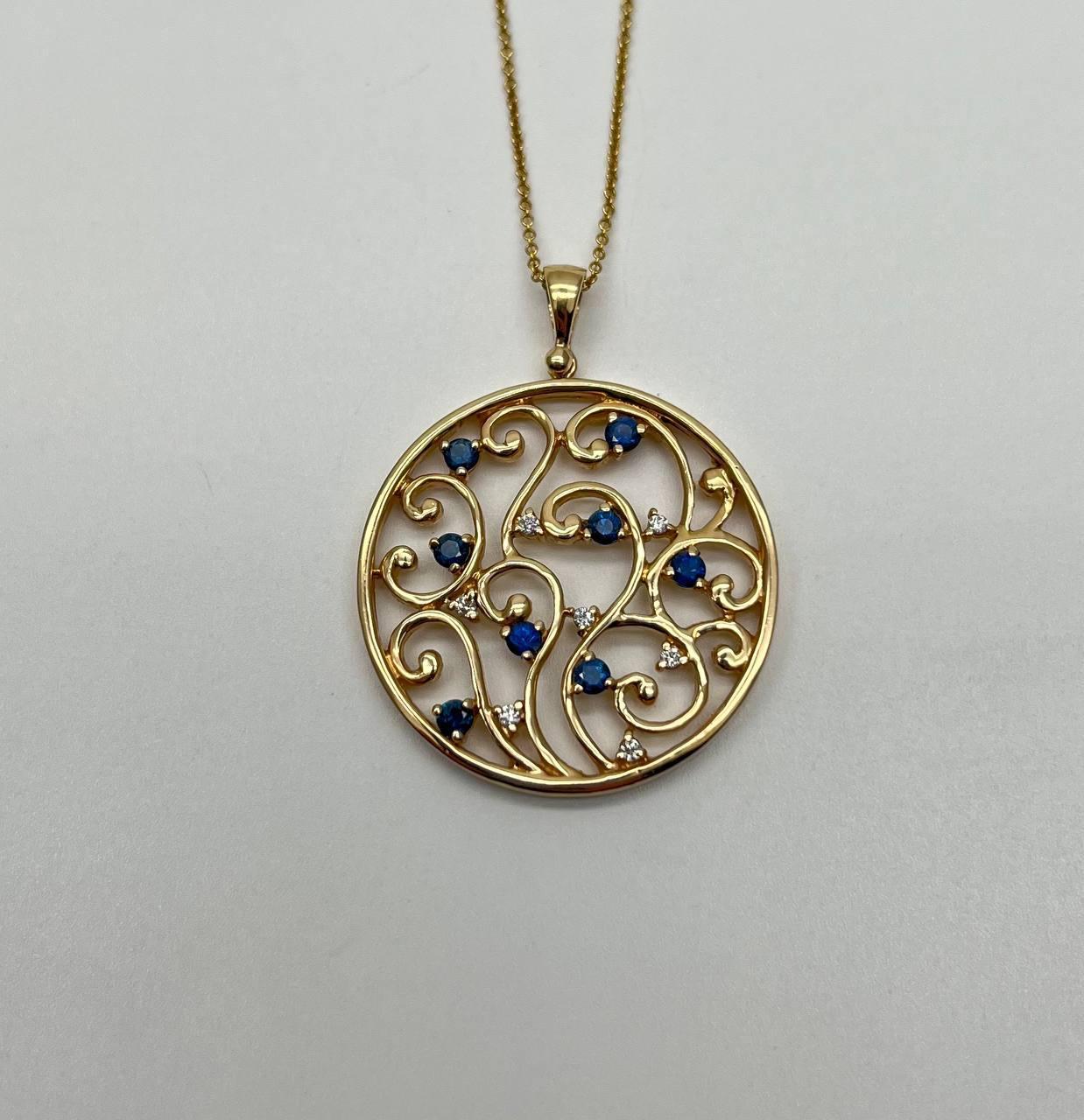 This elegant 21st-century pendant, crafted by Galt & Bro. Jewelers, features a captivating openwork design with intricate swirling patterns. Adorned with vibrant blue gemstones and sparkling white accents, the piece exudes a sense of refined