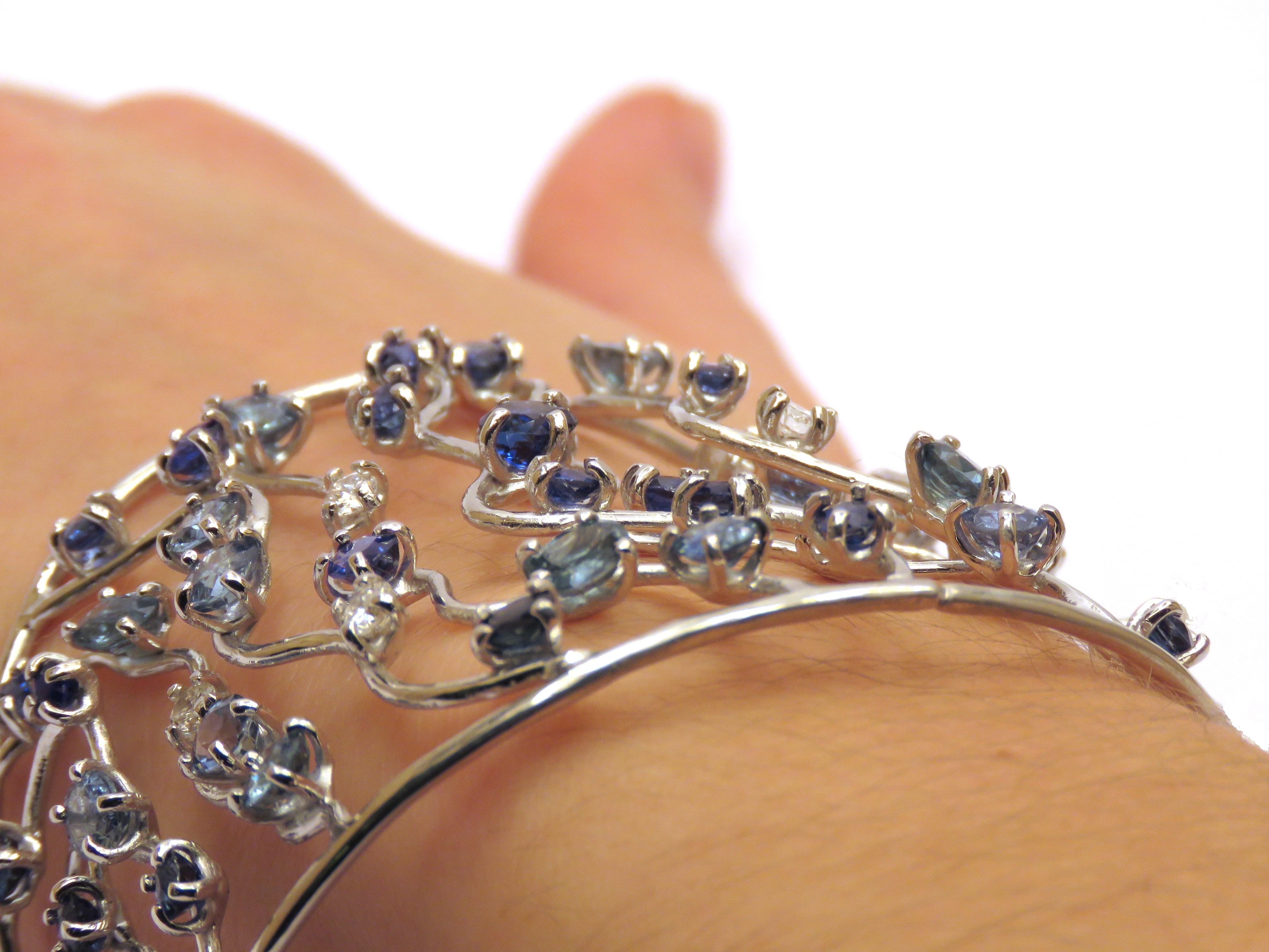 Breath-taking cuff bracelet inspired by the harmonious grace of ocean waves handcrafted in 18 karat white gold. Depicting waves throughout each of the stems, the bracelet is dotted with 65 vibrant blue sapphire gemstones in multiple shades totalling