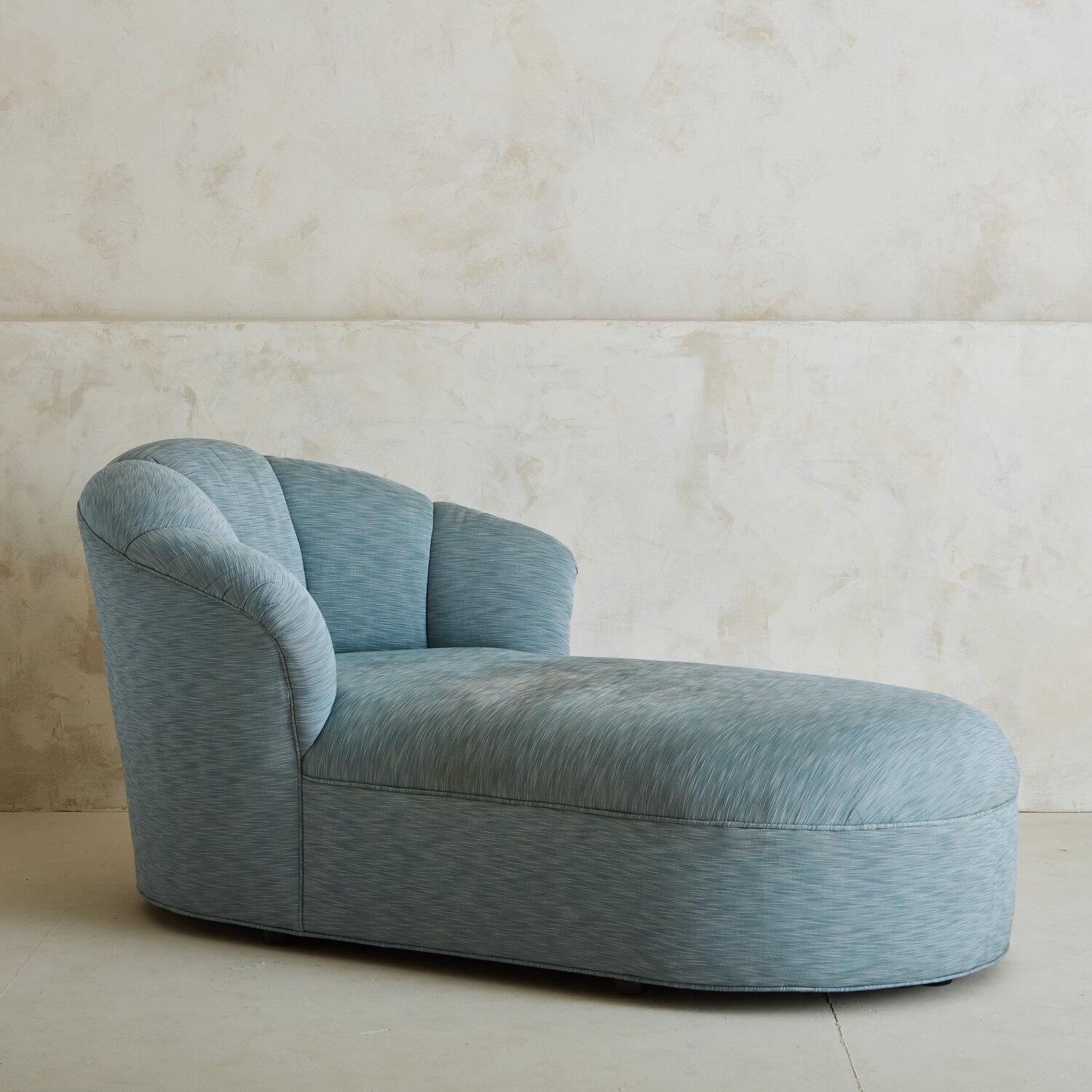 A long, curvaceous chaise lounge featuring a rounded scalloped back that extends upwards from the base. This chaise has a contemporary silhouette and sits just above the ground. It would look fabulous in a bedroom or reading nook.