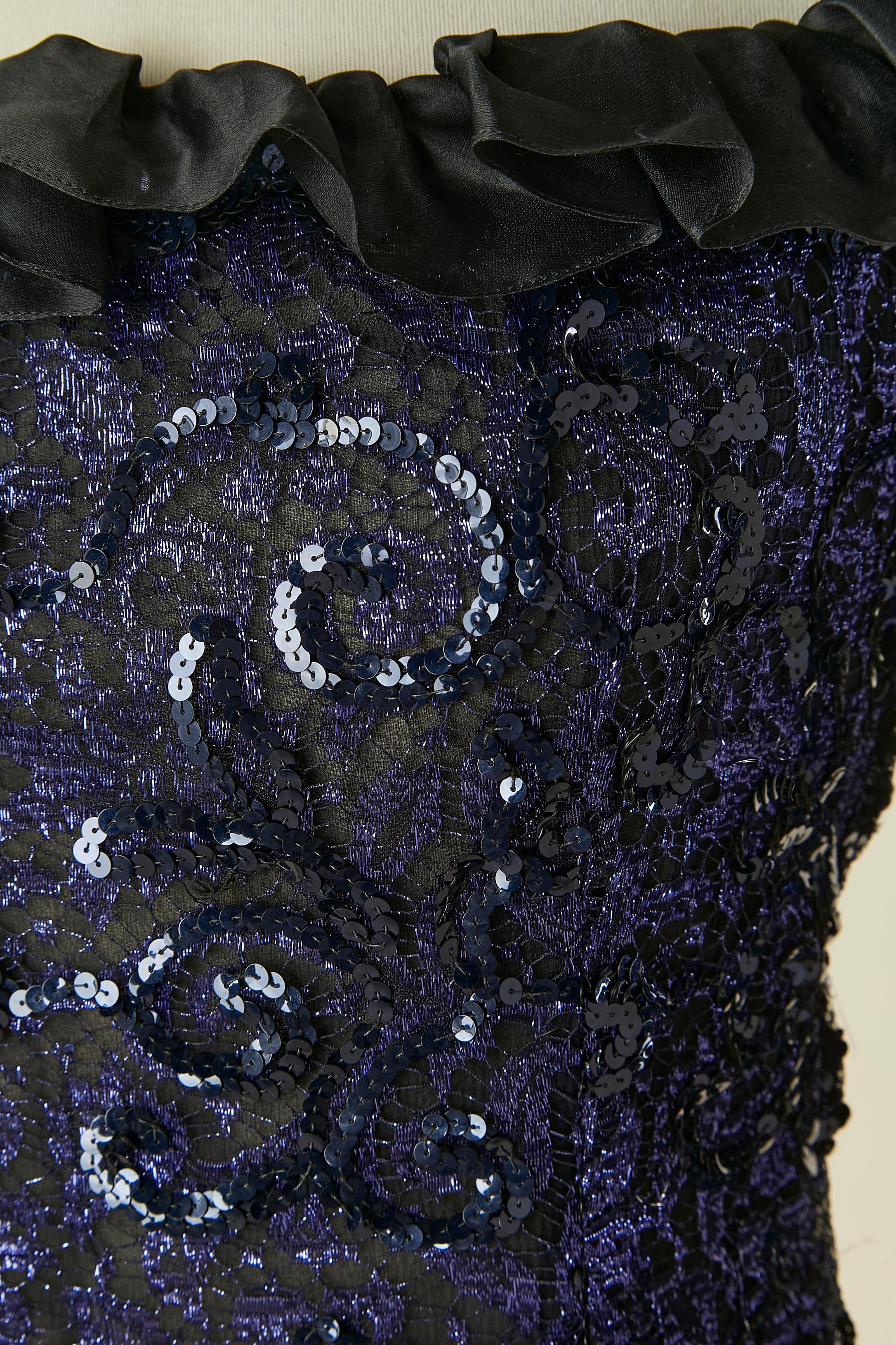 Abito blu in paillettes e pizzo con volant in organza di seta nera. 
Chiusura con zip sul lato sinistro.
TAGLIA 38 (Fr) M 