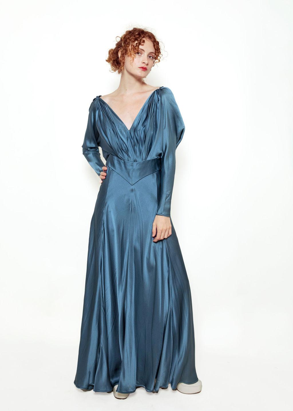 Feel like a princess in this one-of-a-kind blue silk gown!

Featuring a deep v neck, open cross strap back, and ruched neck detailing, this gown is ultra-flattering from the front and jaw-dropping from the back thanks to the lovely rosettes. This