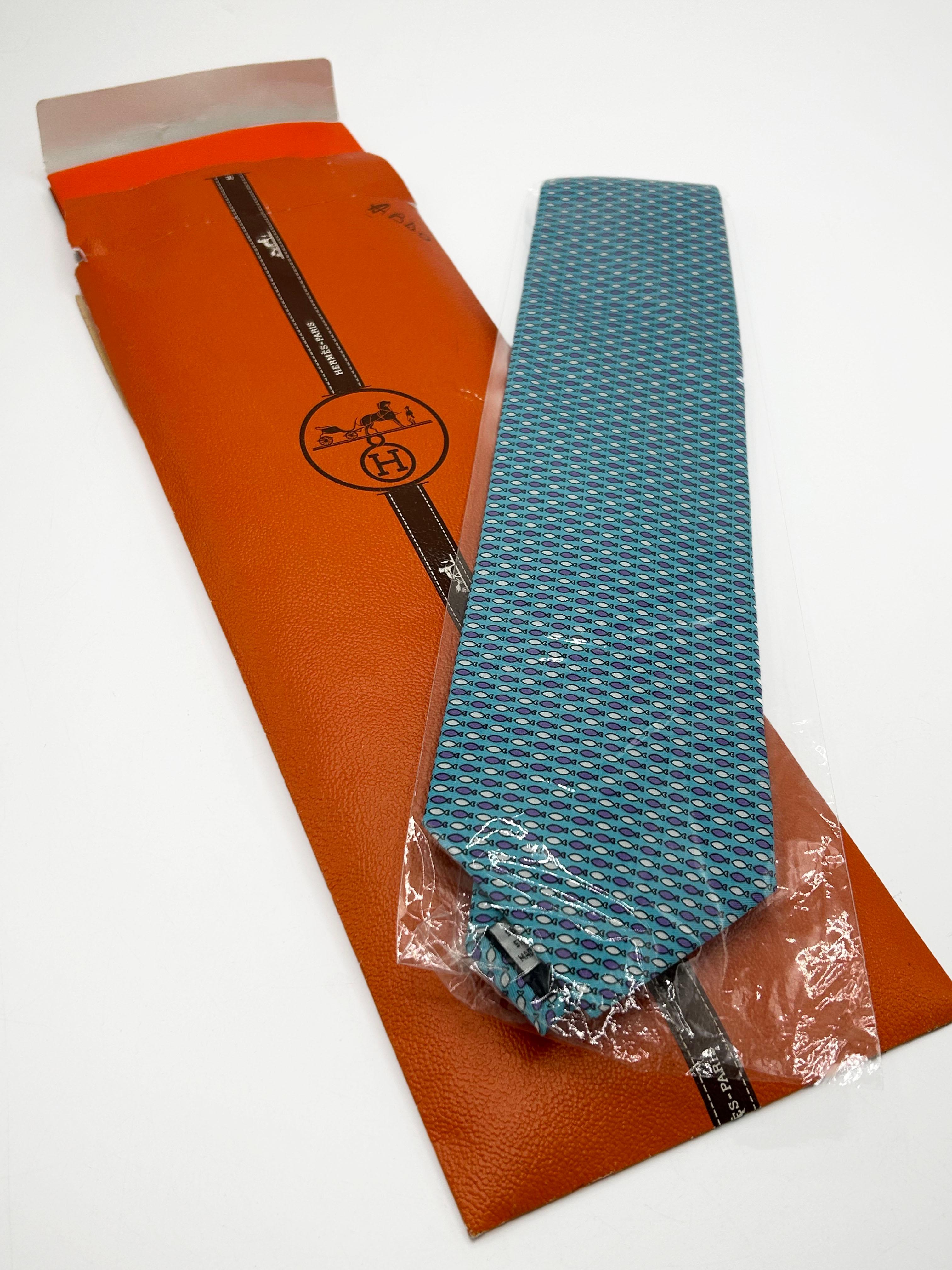 Blue Silk Tie with Hermès Paris Print
This sky blue Hermès silk tie features a detailed, repeating pattern of small stylized fish in white and purple. The design incorporates the brand's signature 