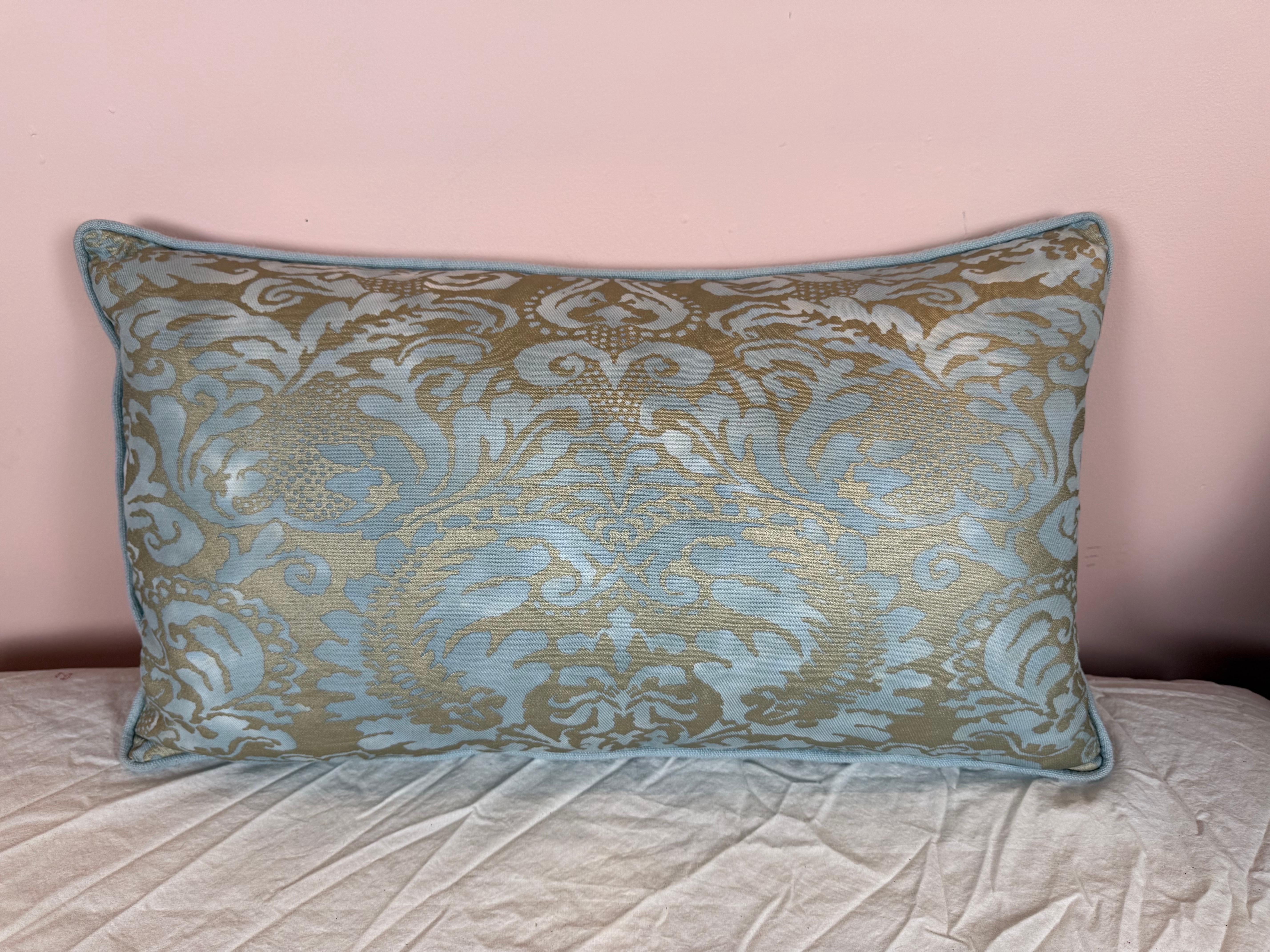 This sophisticated Fortuny pillow features an intricate damask pattern in a soft, shimmering blue and muted gold palette. The fabric’s subtle sheen highlights the ornate design, which includes scrolling foliage and stylized florals—hallmarks of