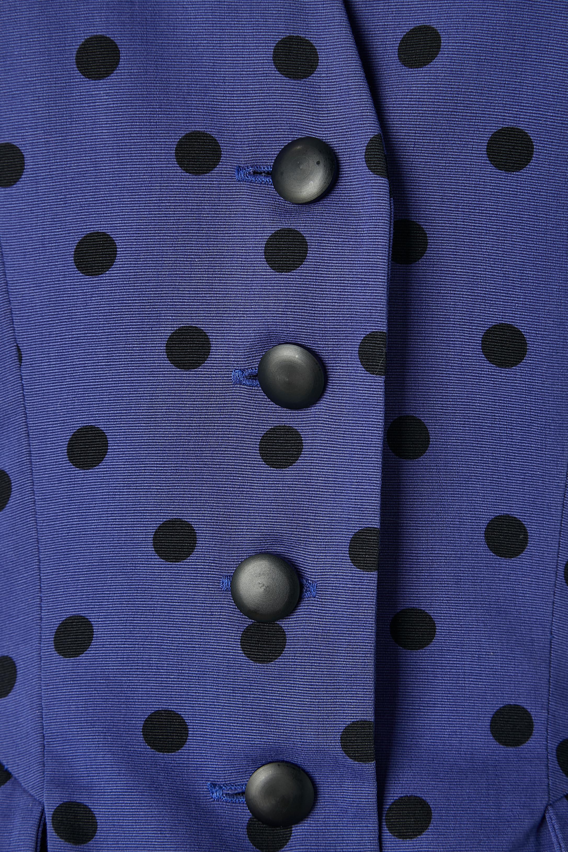 Falda-traje azul con lunares negros. Composición del tejido principal: 100% algodón. No se indica el forro, pero probablemente sea de rayón o acetato. 
Cierre de botón y ojal en el centro delantero. Hombreras. 
TALLA 42 (Fr) M