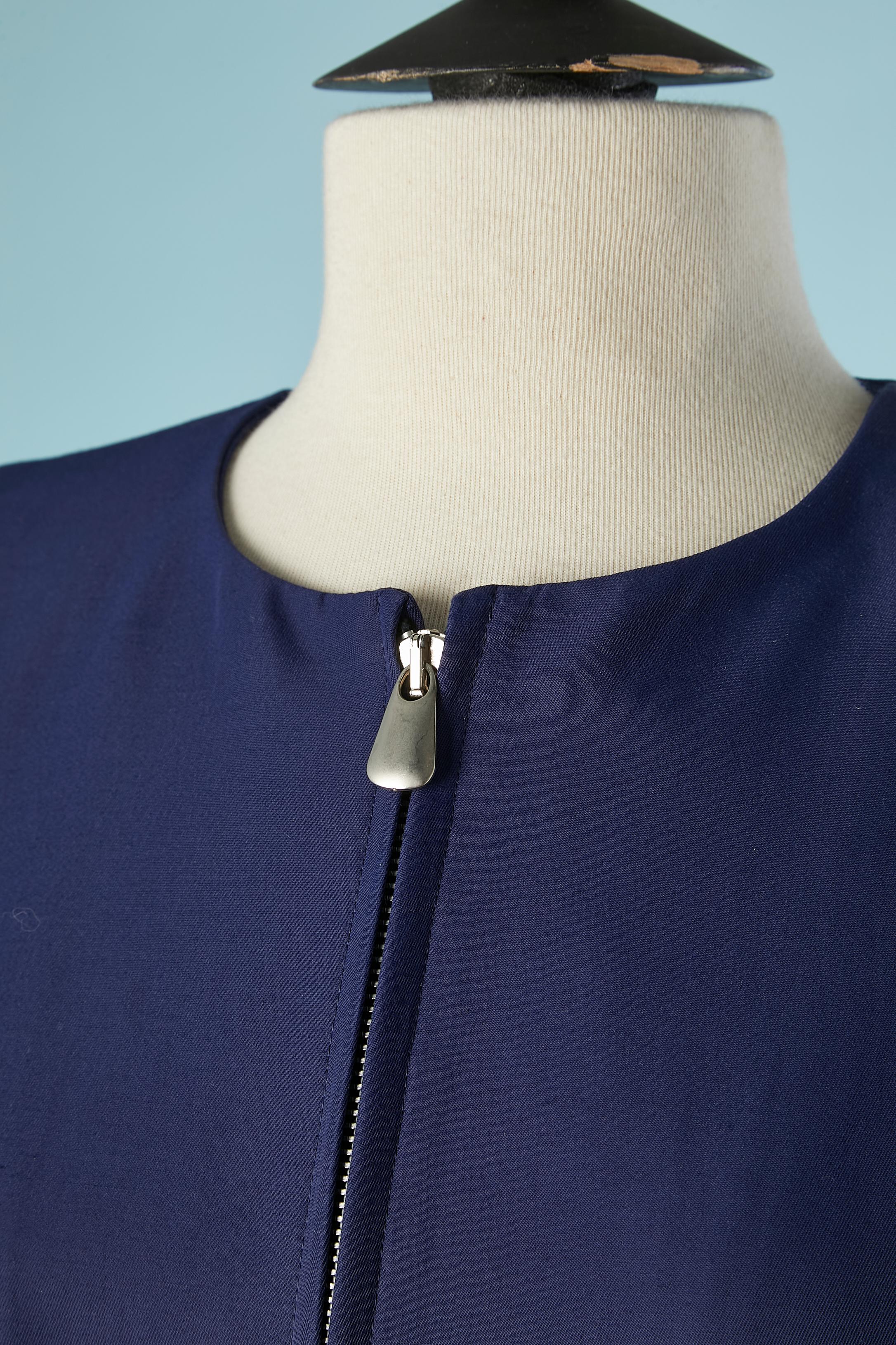 Combinaison jupe bleue avec fermeture à glissière au milieu du devant. Poche zippée également. Pad d'épaule. 
Composition du tissu principal : 62% coton, 38% polyamide. Doublure : 63% acétate, 37% rayonne. 
Ceinture sur la jupe avec boucle en métal