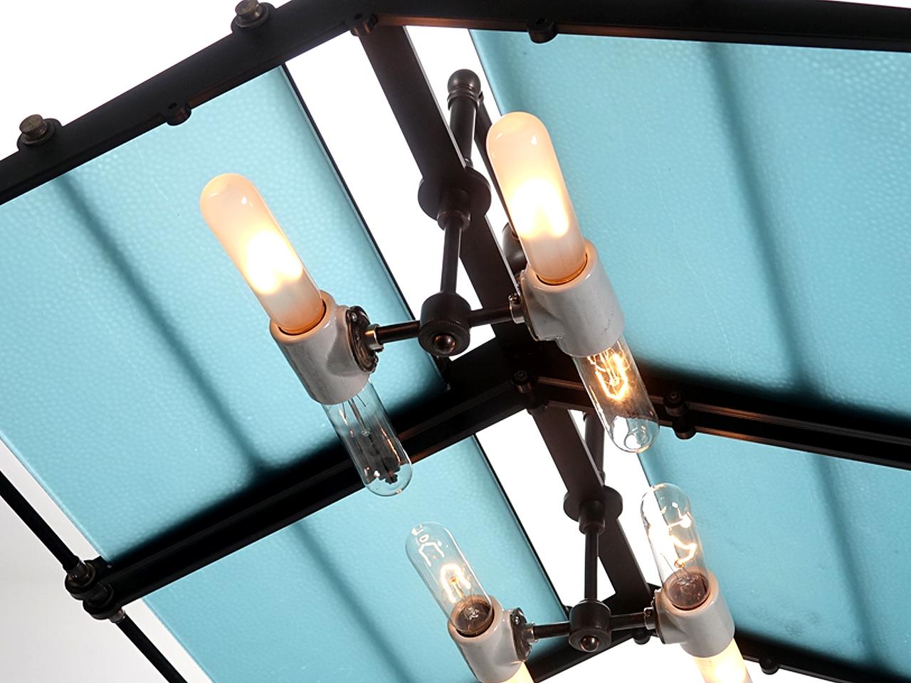 This oversized chandelier features a substantial 24 x 24 inch frame designed for the rare antique blue pebbled glass. The glass casts a beautiful 3D glow. The blackened brass and steel frame tents over four floating horizontal tubular bulbs using