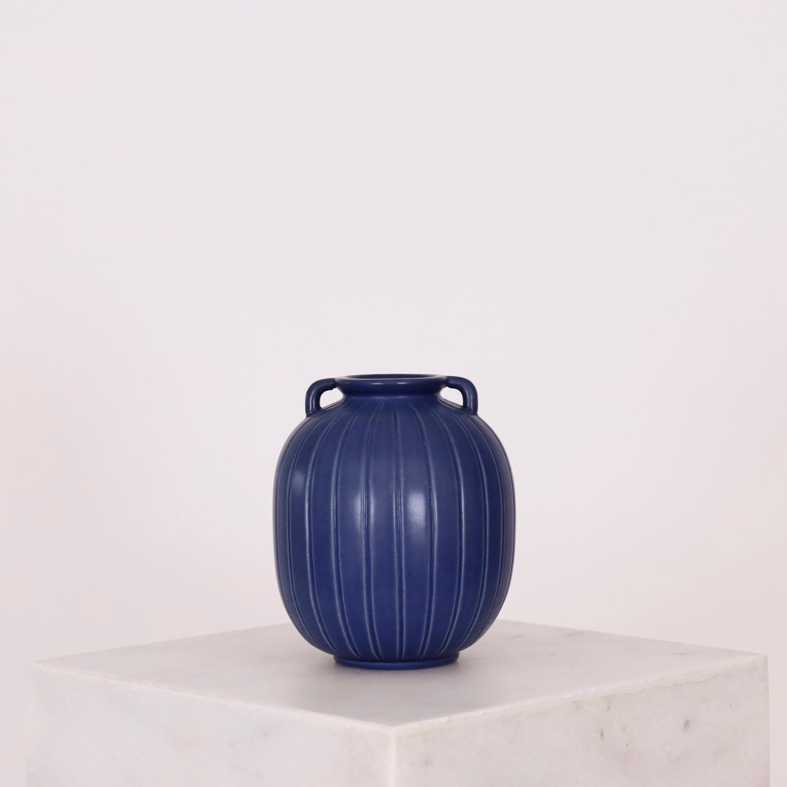 A blue stoneware vase with vertical lines designed by Axel Sørensen for P. Ipsens Enke in 1941. Simple, yet exquisite.  

* A blue stoneware vase with vertical lines and small handles.
* Designer: Axel Sorensen
* Style: 14
* Producer: P. Ipsens