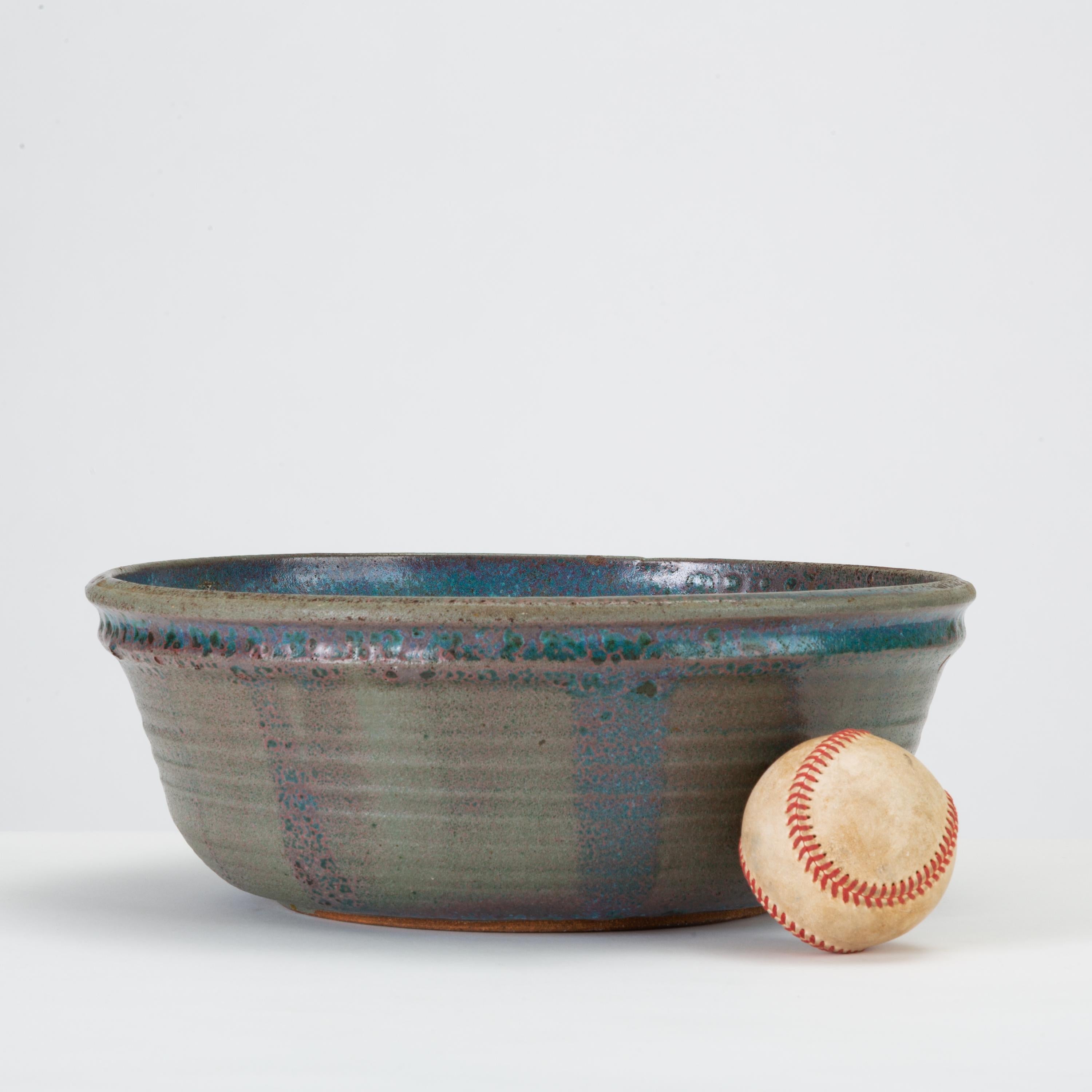 A wheel-thrown studio pottery bowl with a flat bottom and steep sides. A double lip is highlighted by a vibrant strip of cobalt glazing; the bowl is glazed all over in a deep blue with lighter speckled accents. Subtle blistering adds a rustic