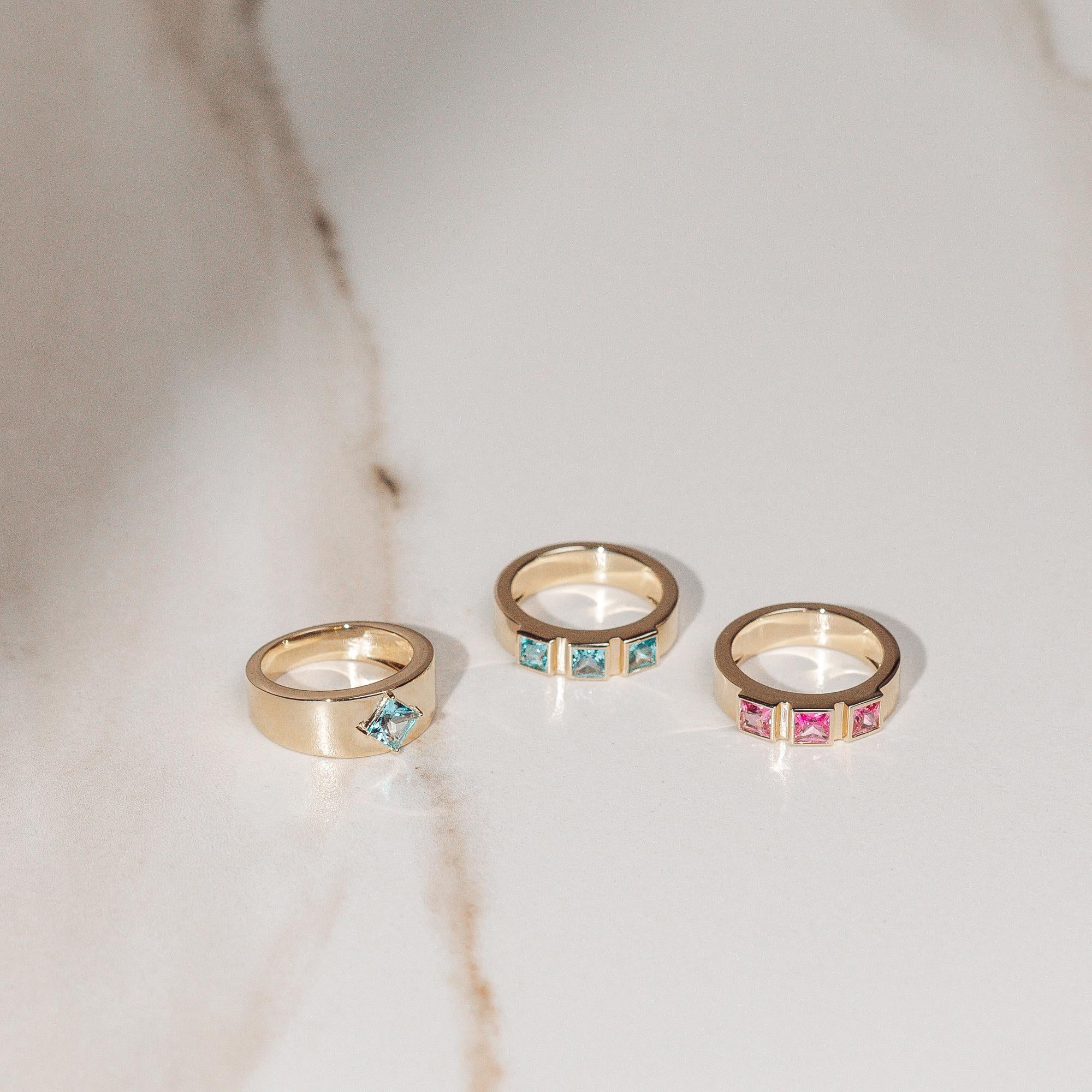 Setzen Sie ein kühnes, aber elegantes Statement mit diesem atemberaubenden, fein gearbeiteten 3-Stein-Ring aus Blautopas. 3 große blaue Topase im Prinzess-Schliff entsprechen 1,237 ctw und sind in 14k Gelbgold eingefasst. Die Nachfrage nach