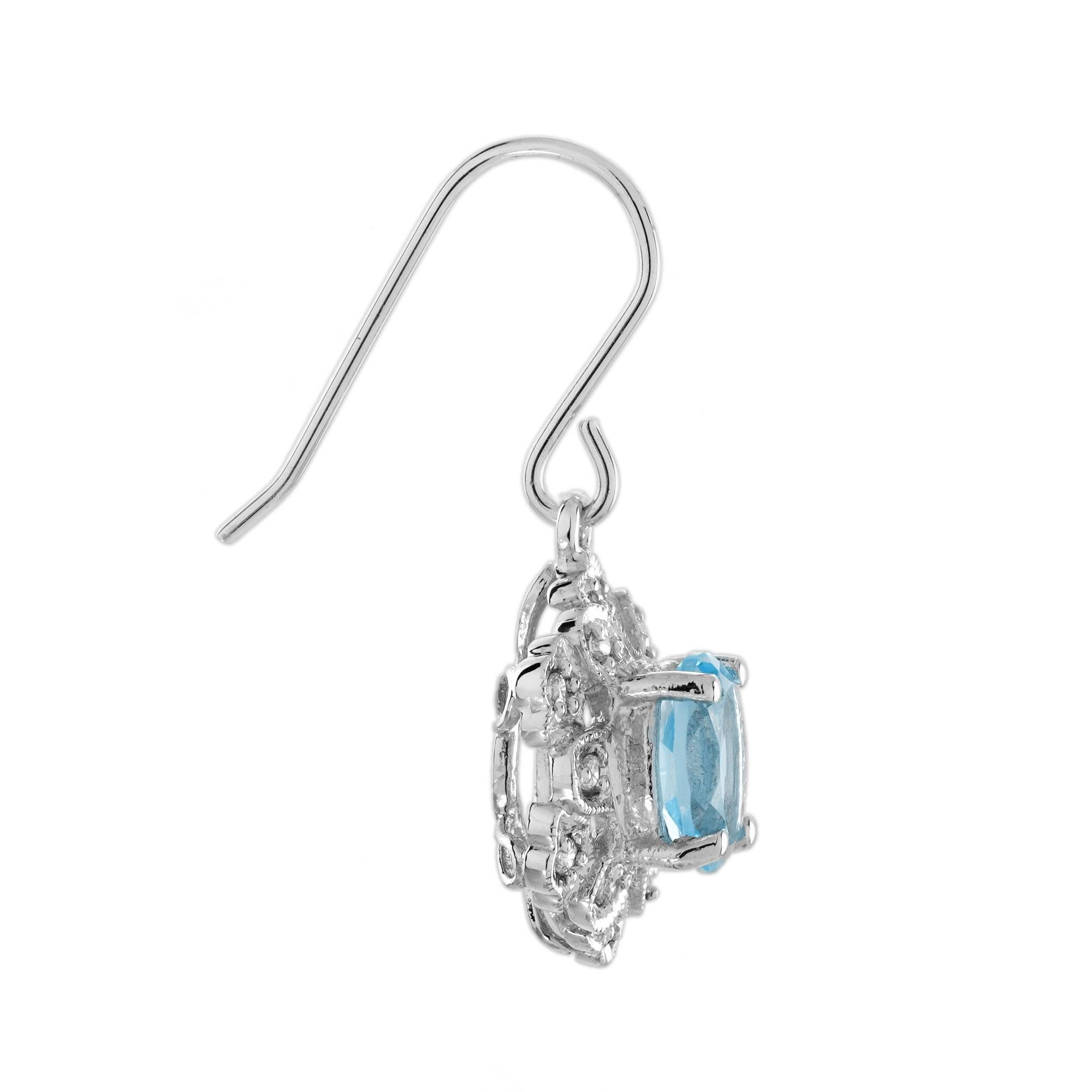 Inspirées par le glamour de l'époque Art déco, ces boucles d'oreilles présentent une topaze bleue de taille ovale sertie dans des griffes sécurisées et encadrée d'un halo de diamants scintillants. La pierre précieuse vibrante et les accents