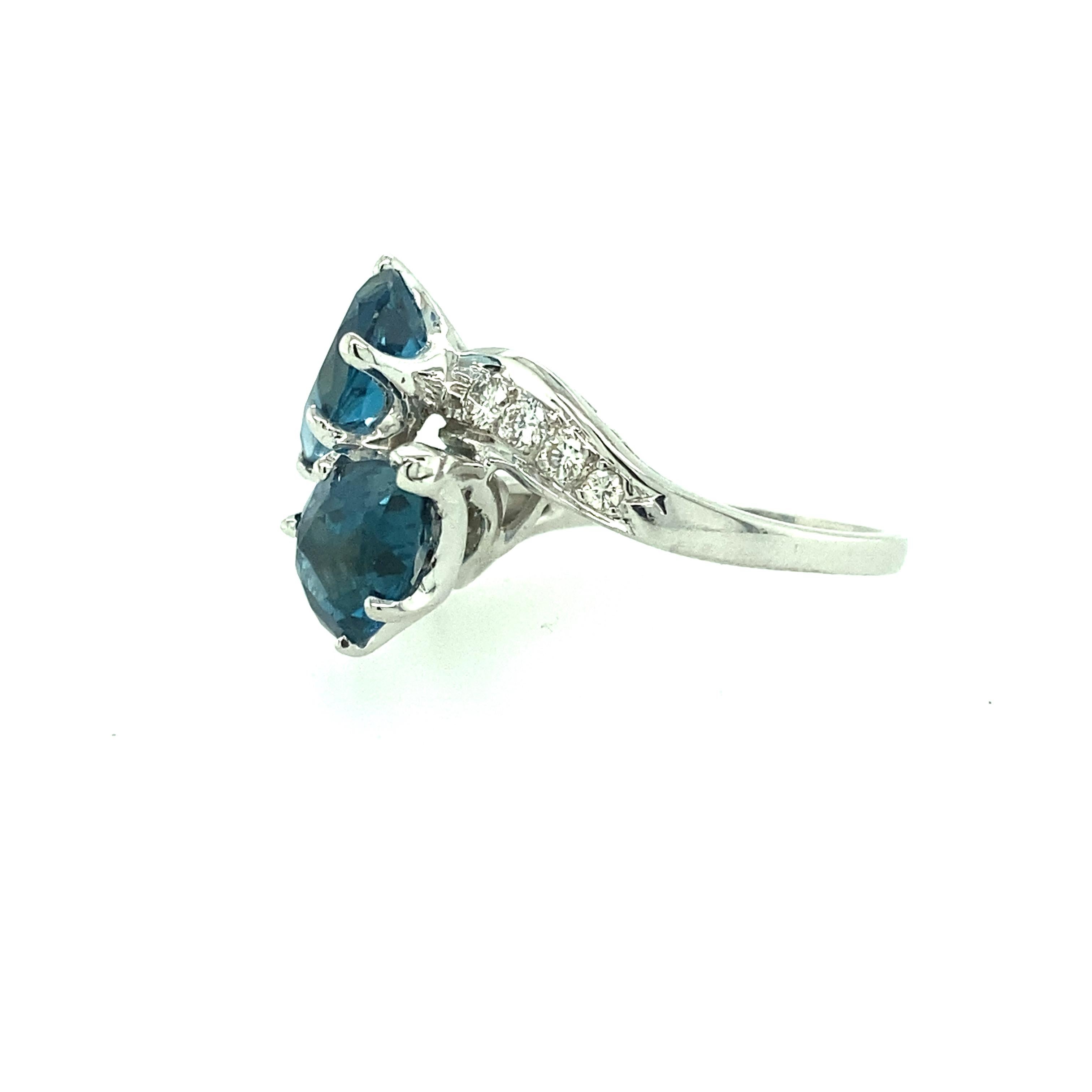 One 14 karat white gold estate ring set with two 7.5x10mm pear shaped blue topaz and eight brilliant cut diamonds, 0.20 carat total weight with matching H/I color and SI clarity. The shank measures 8.30mm near the top of the ring and tapers to 1.60