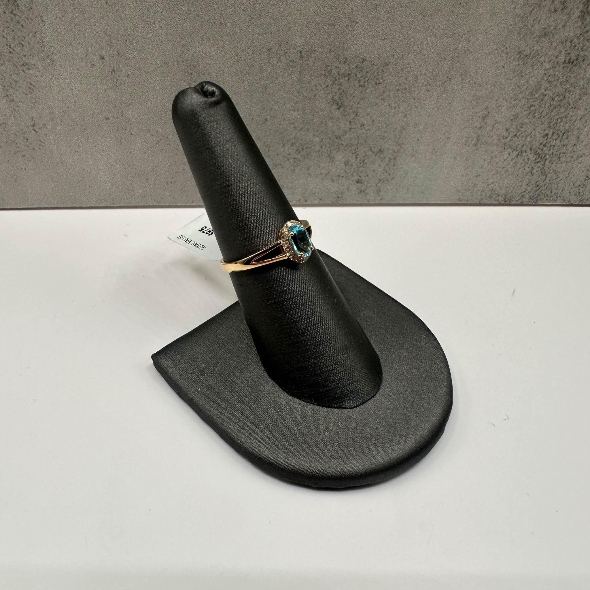 Cette magnifique bague en or jaune 14kt ornée d'une topaze bleue ovale de 6x4 mm est complétée par 0,09ctw de diamants ronds de taille unique SI2-I1, ajoutant une touche d'éclat à la pierre précieuse vibrante. De taille 6,5, il s'adapte