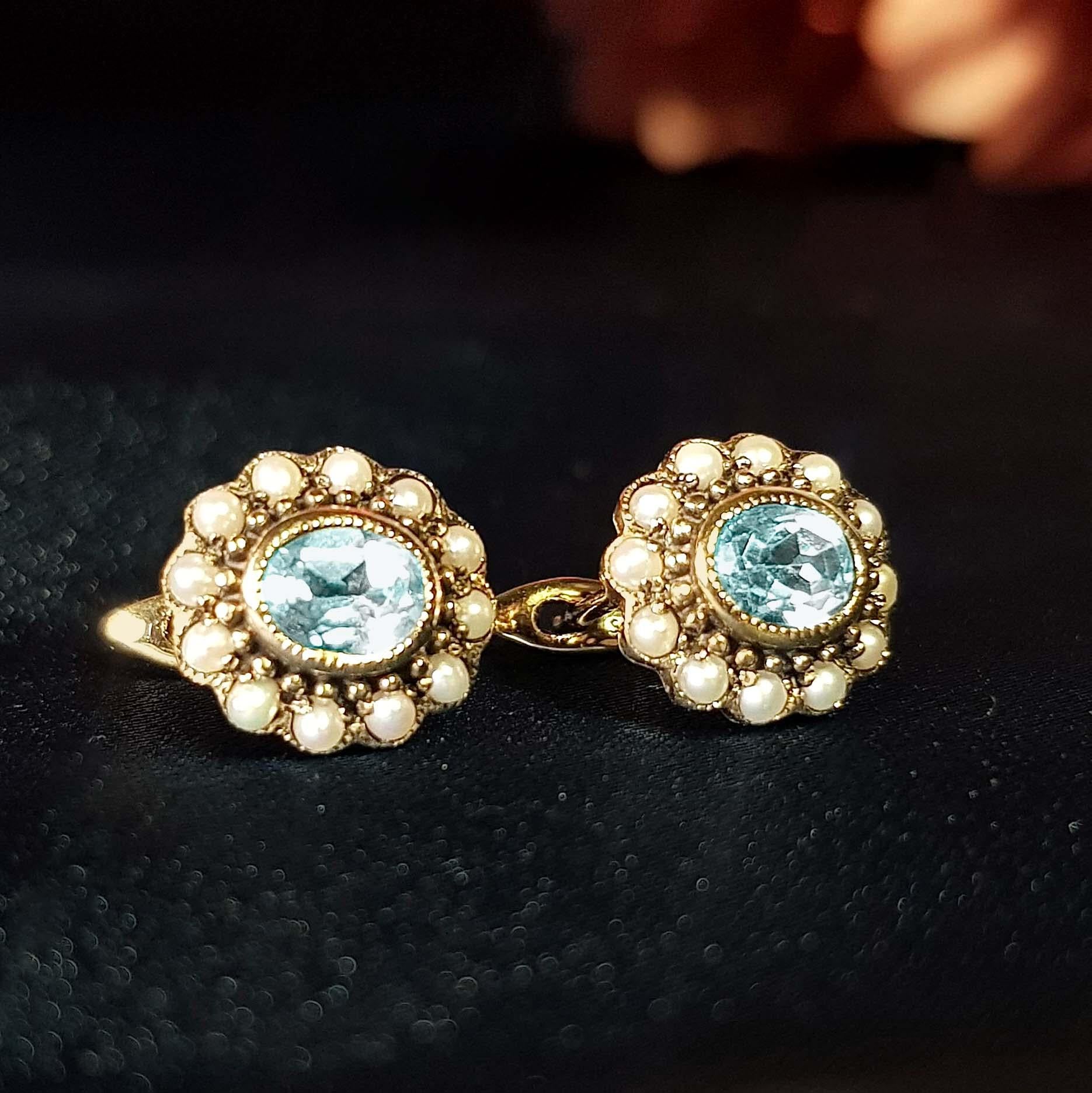 Un sorprendente paio di orecchini con topazio blu e perle in stile vintage per orecchie forate. Ogni orecchino presenta un topazio blu dal taglio ovale circondato da un'aureola di perle d'acqua dolce in una montatura a grappolo. Sono l'accessorio