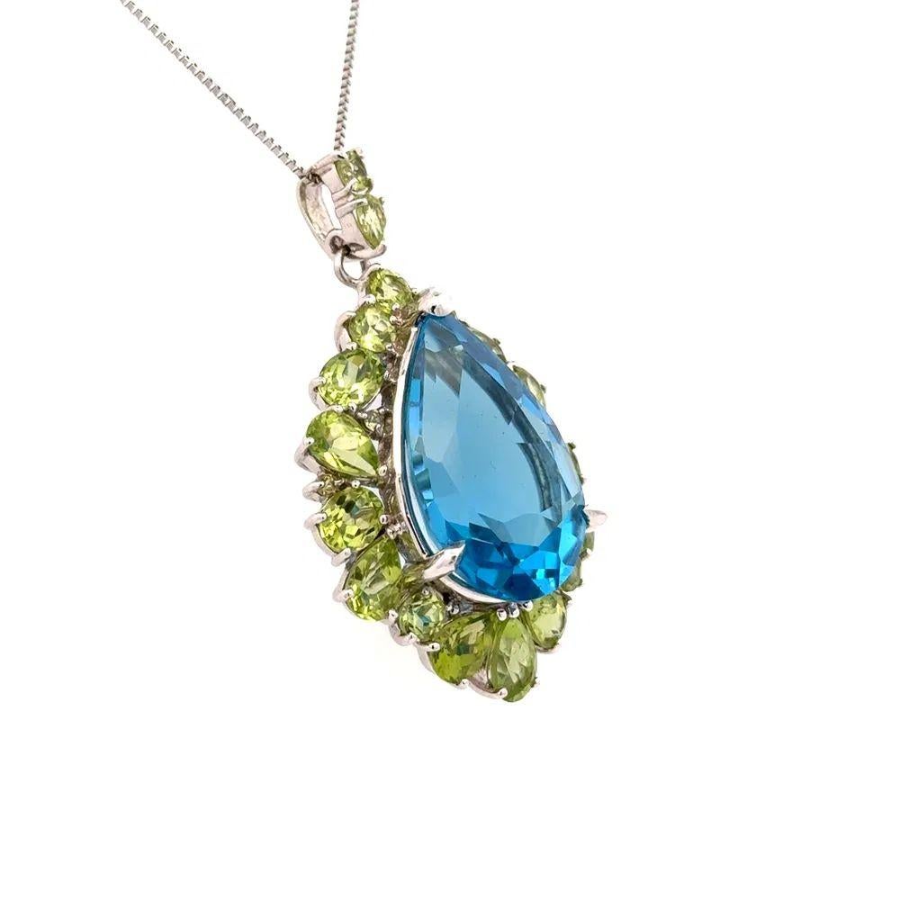 Simply Beautiful! Blue Topaz and Peridot Gold Drop Pendant Necklace. Cantering a securely Hand set Pear Blue Topaz, weighing approx. 18 Carats. Surrounded by Peridot, approx. 18.97tcw. Wow! Hand crafted 14K White Gold mounting. Suspended from a