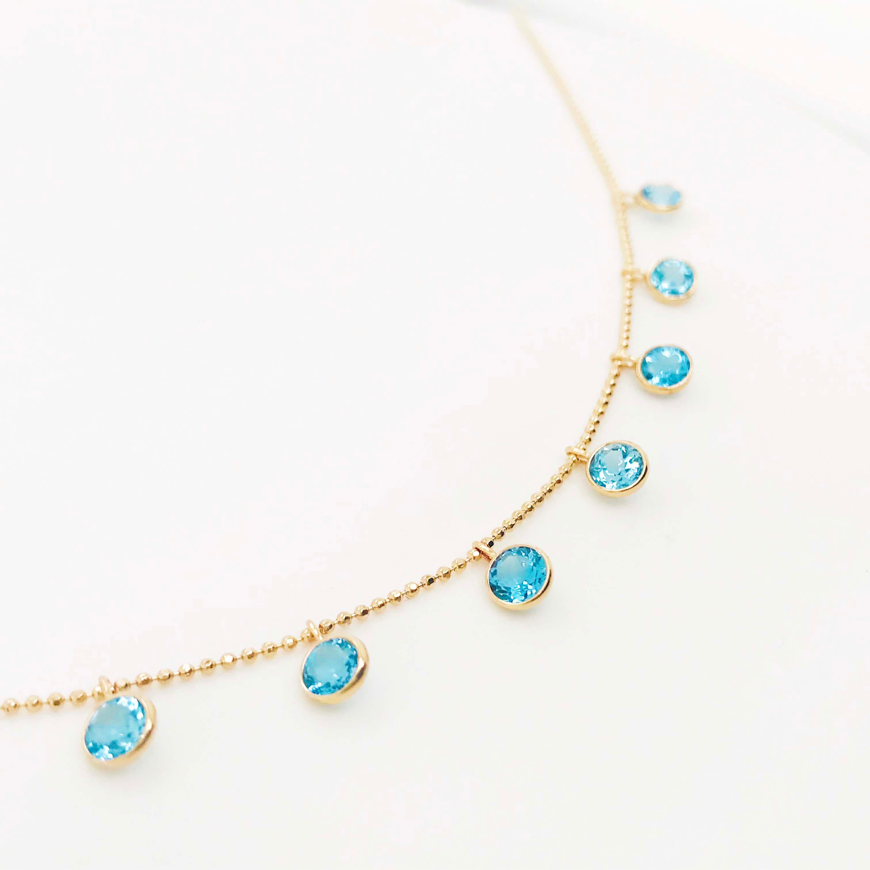 Adorable blue topaz gemstone charm necklace! This necklace is a modern design with 9 round blue topaz gemstones weighing 2.25 carats total weight and set in gold bezels that dangle on a gold beaded chain. The bezel charms are evenly spaced along the