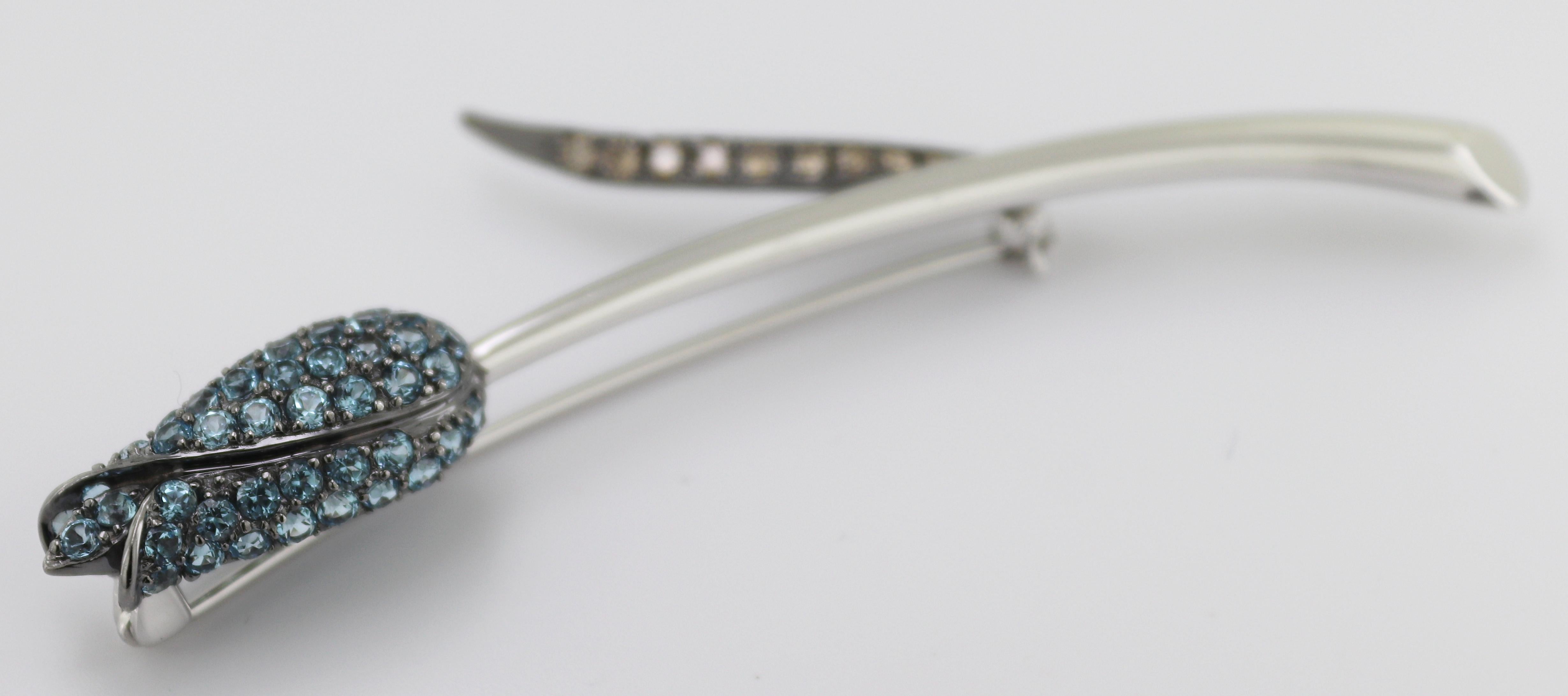 Featuring (54) round-cut blue topaz, accented by (9) full-cut chocolate
diamonds, 0.30 ct, tw., pave set in a blackened, 18k white gold tulip
mounting, 77 X 32 X 10.8 mm, completed by a pin stem and catch, Gross
Weight 8.73 grams.
